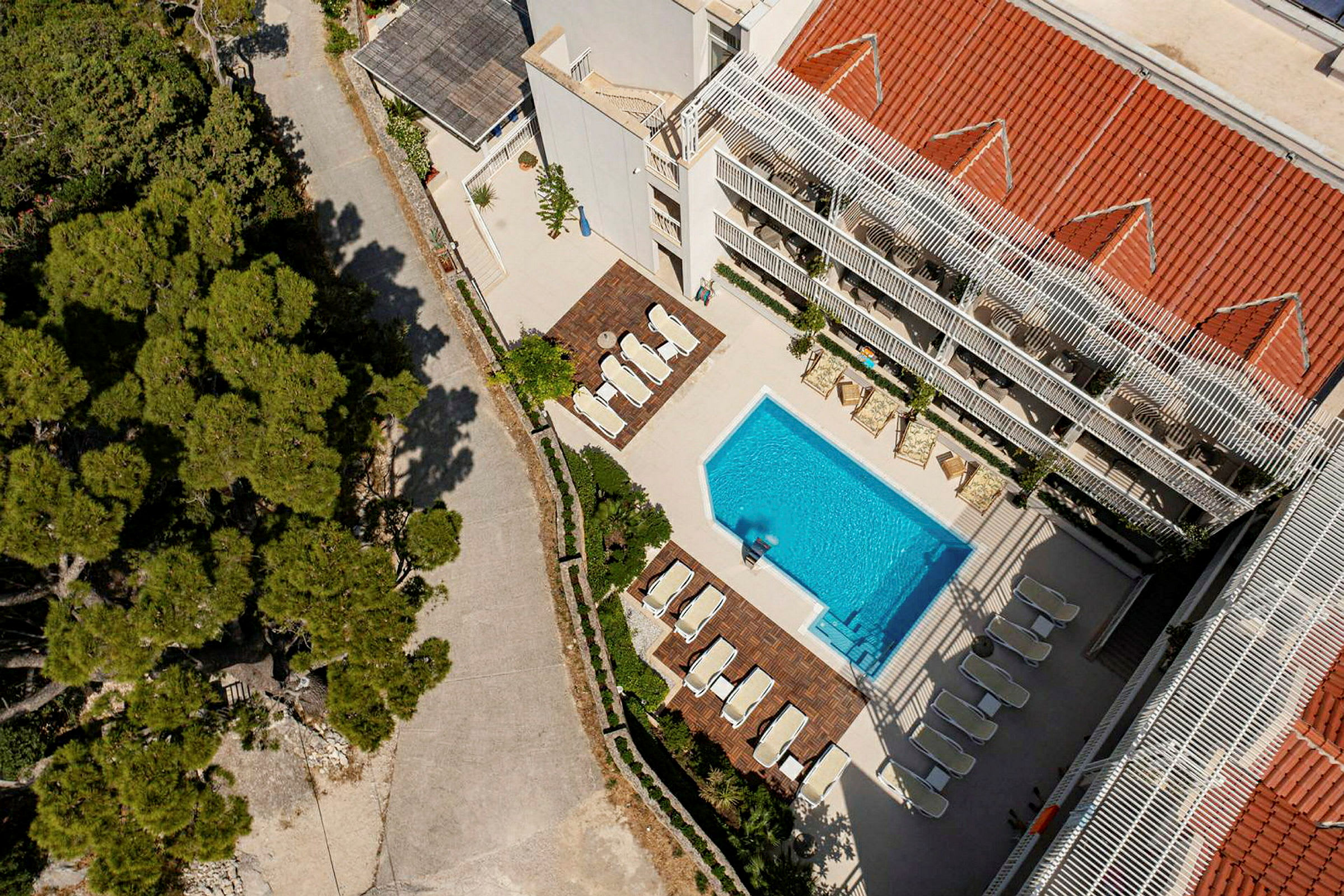 Flygfoto av en byggnad med pool och solstolar, omgiven av träd. (AI-genererad text)