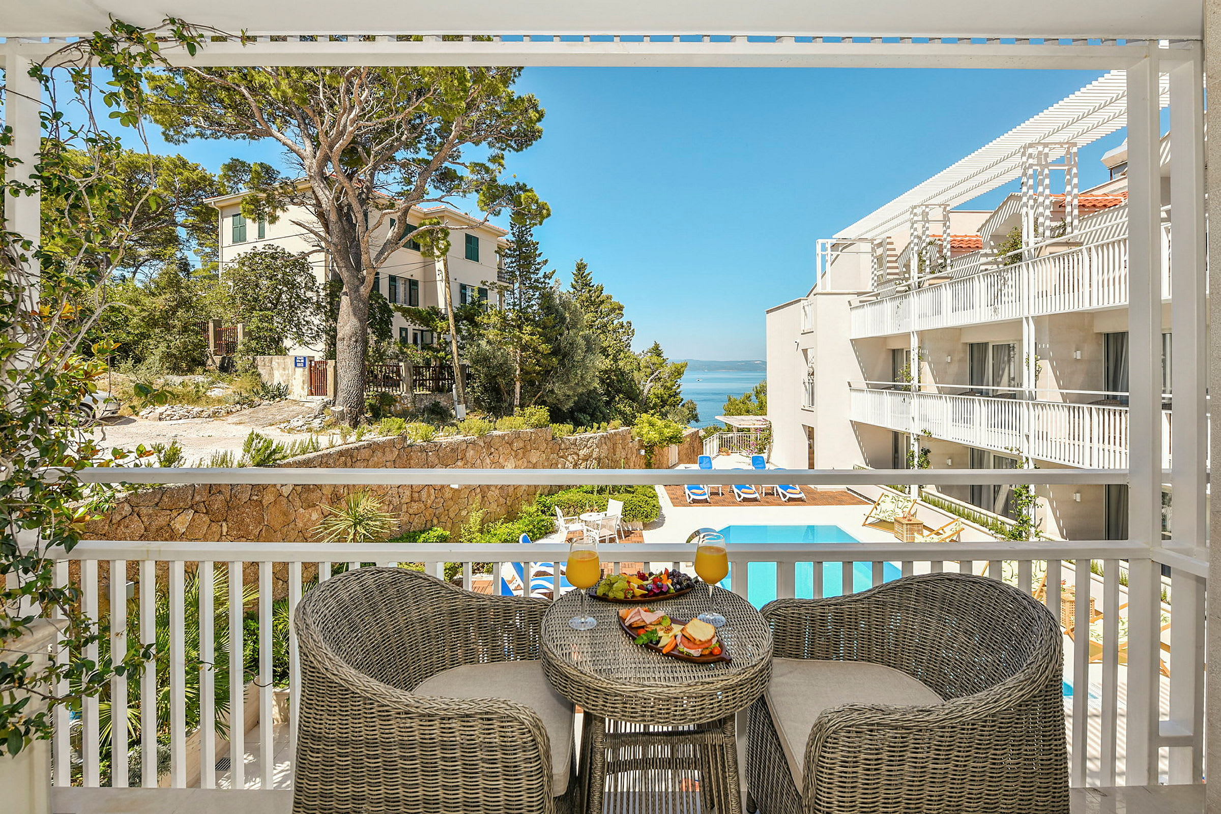 Utsikt från en balkong över en hotellpool och byggnader, med frukost serverad på ett bord. (AI-genererad text)