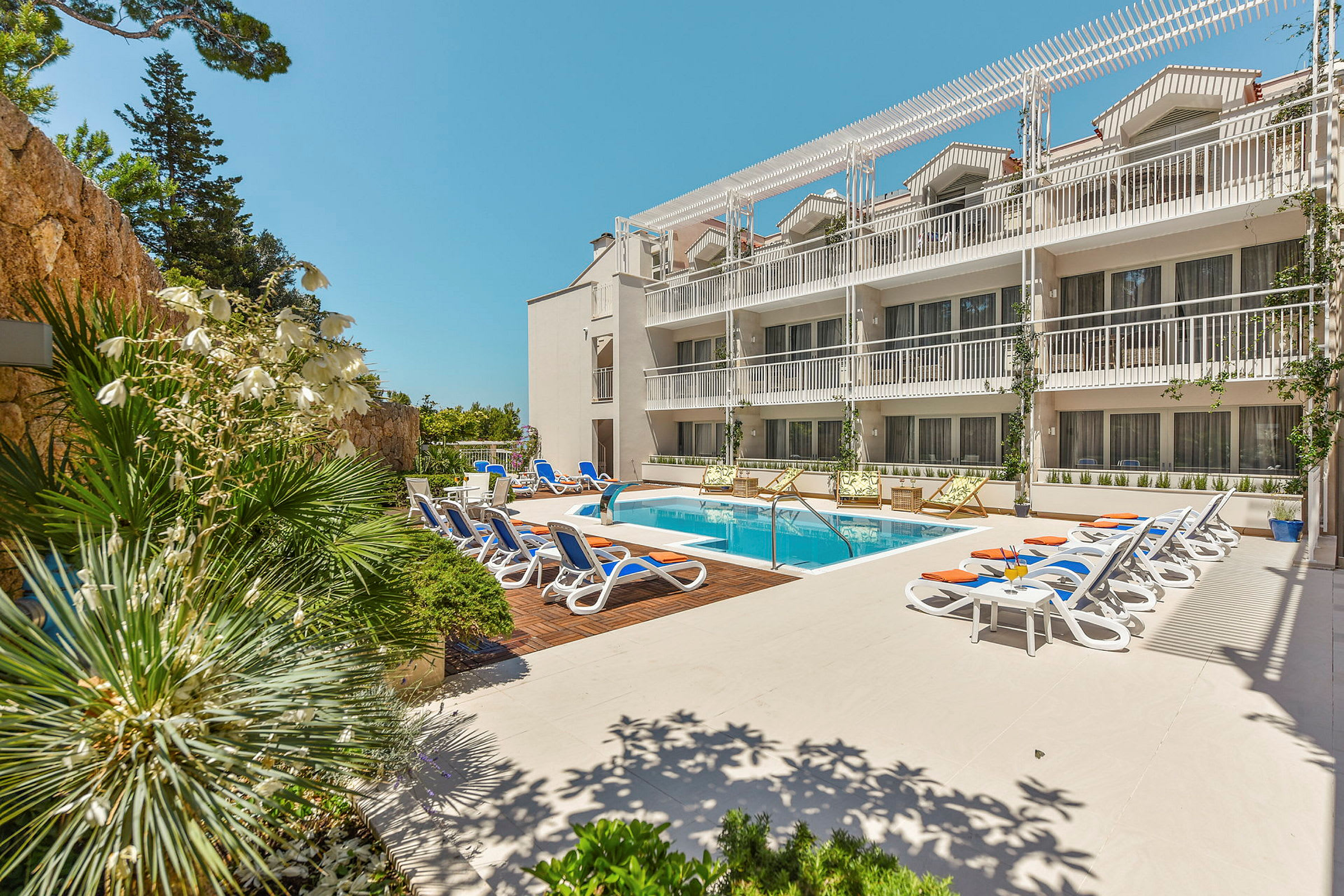 En hotellpool med solstolar och en intilliggande byggnad. (AI-genererad text)