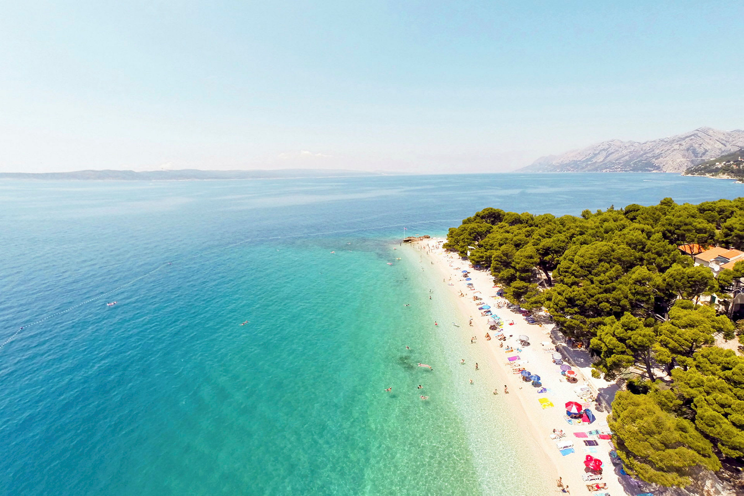 Vit sandstrand med turkost hav och omgivande grönska. (AI-genererad text)