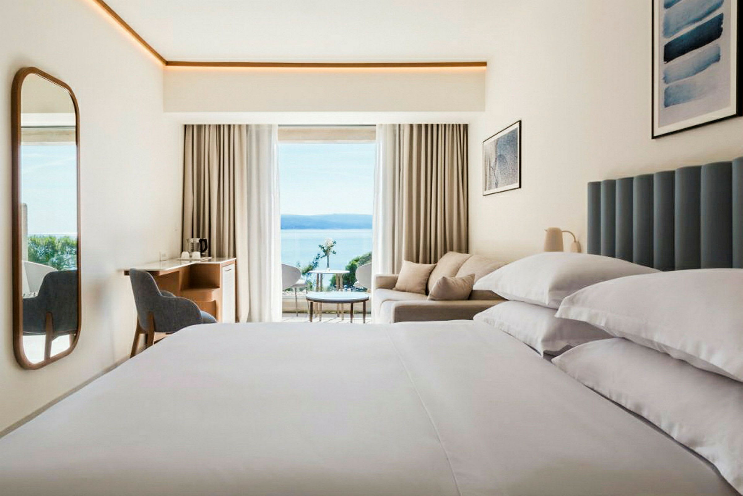 Modernt hotellrum med stor säng, soffa och havsutsikt. (AI-genererad text)
