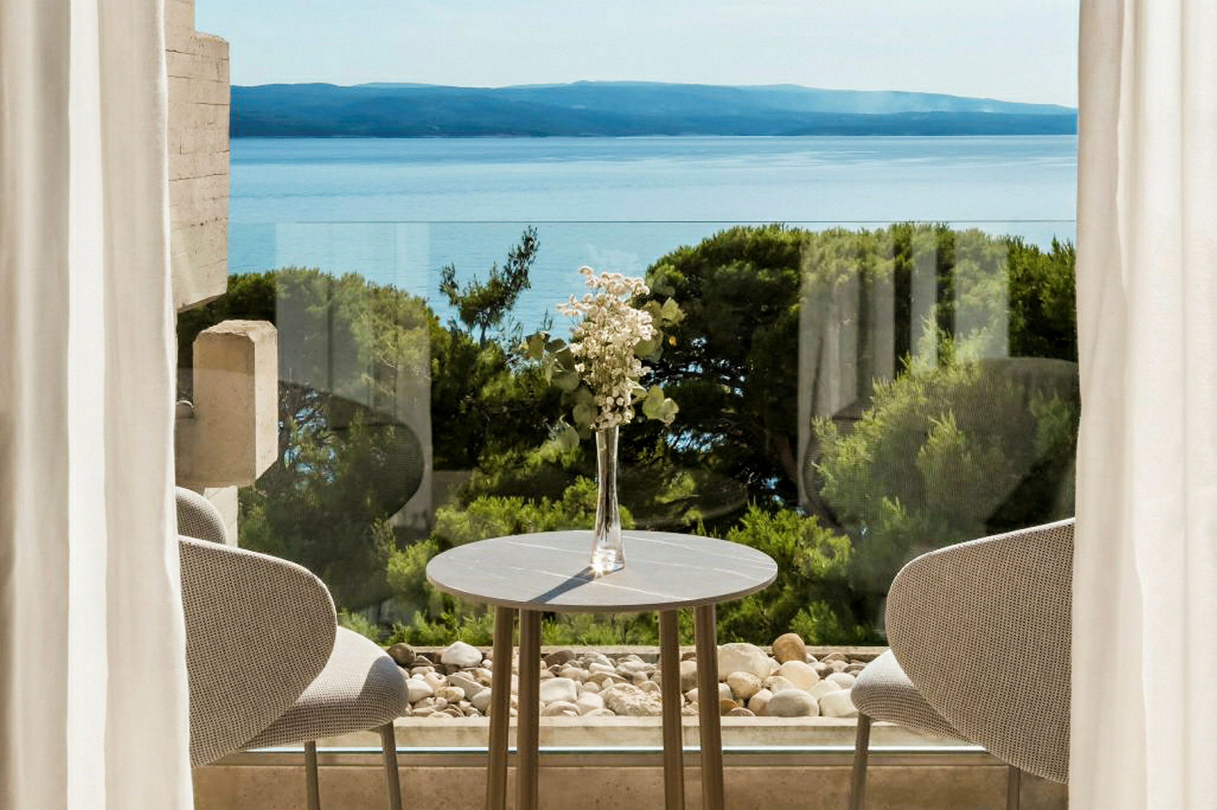 En borddekoration med blommor vid ett bord framför fönster med utsikt över havet och grönska. (AI-genererad text)