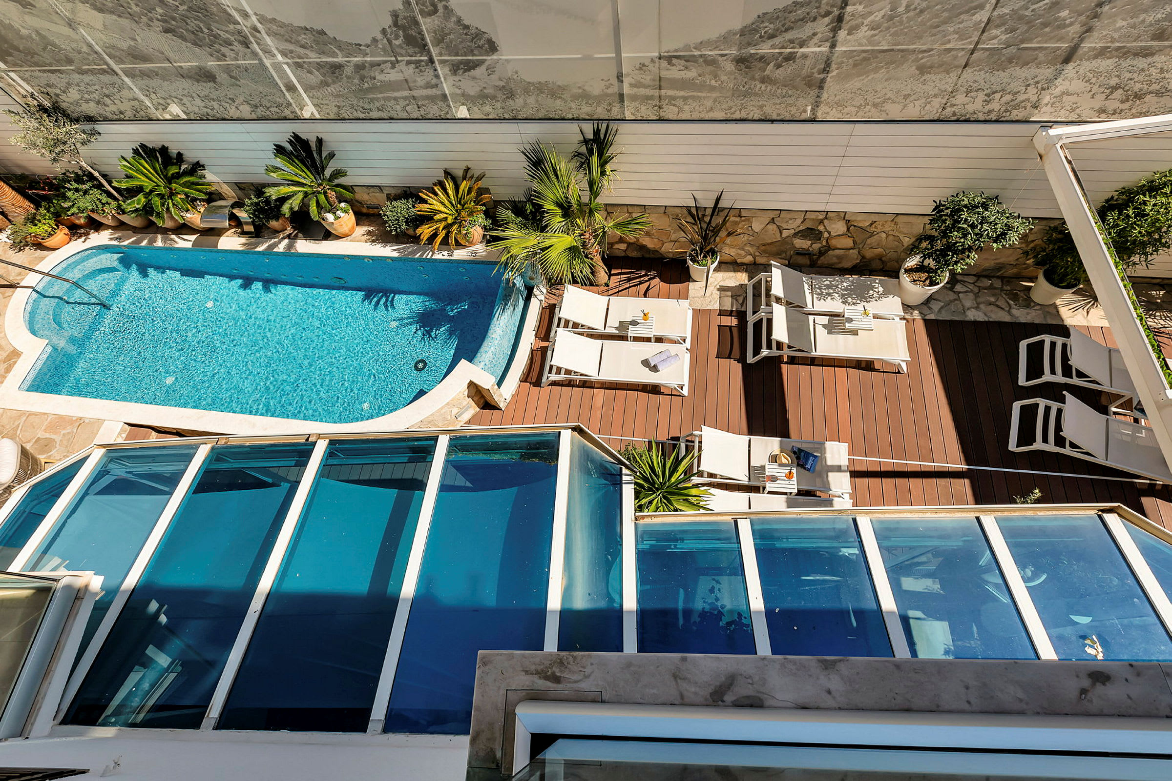En pool och en terrass med solstolar och bord, omgiven av växter. (AI-genererad text)