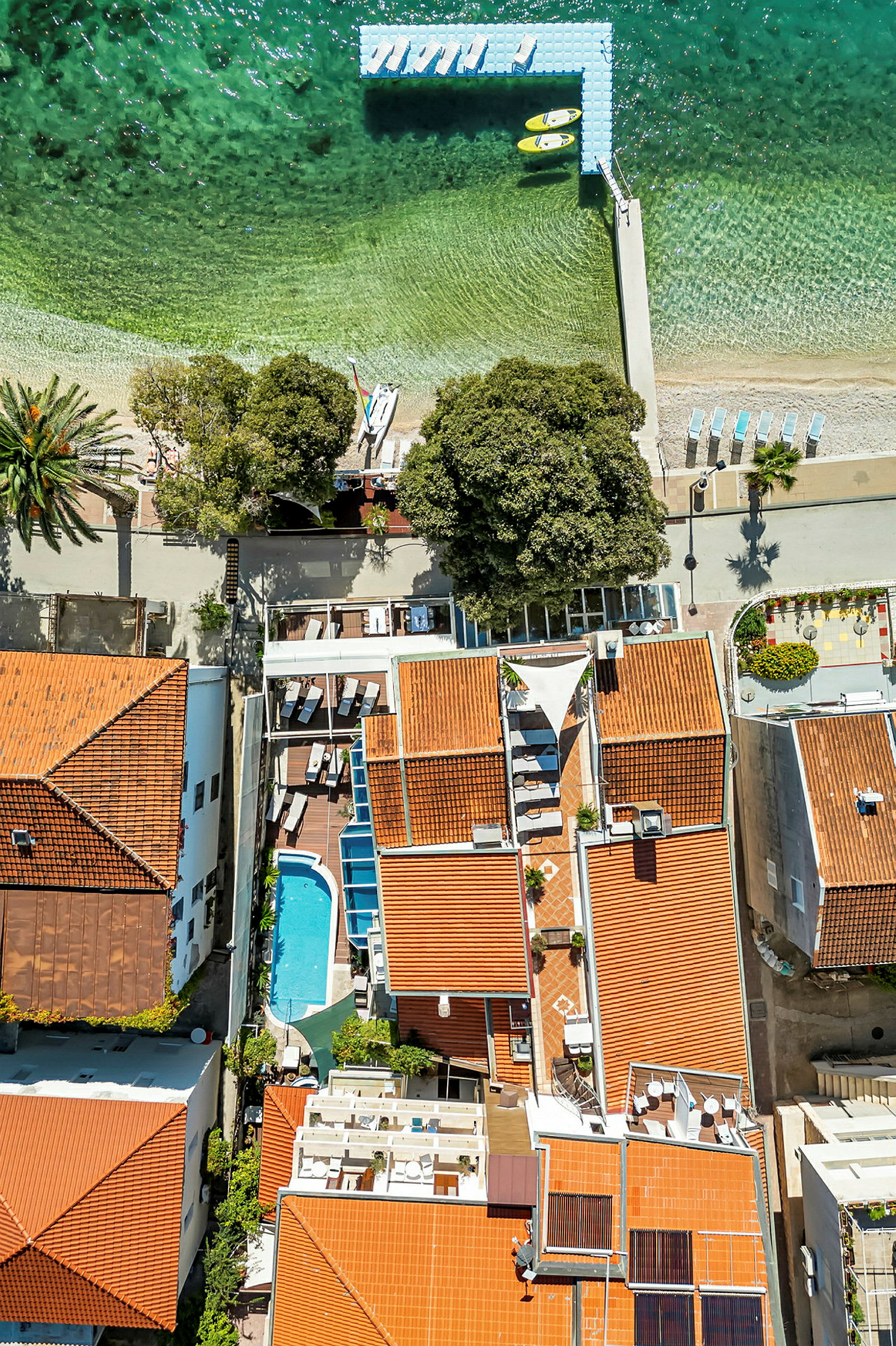 Flygfoto över hustak, en pool och en strand vid havet. (AI-genererad text)