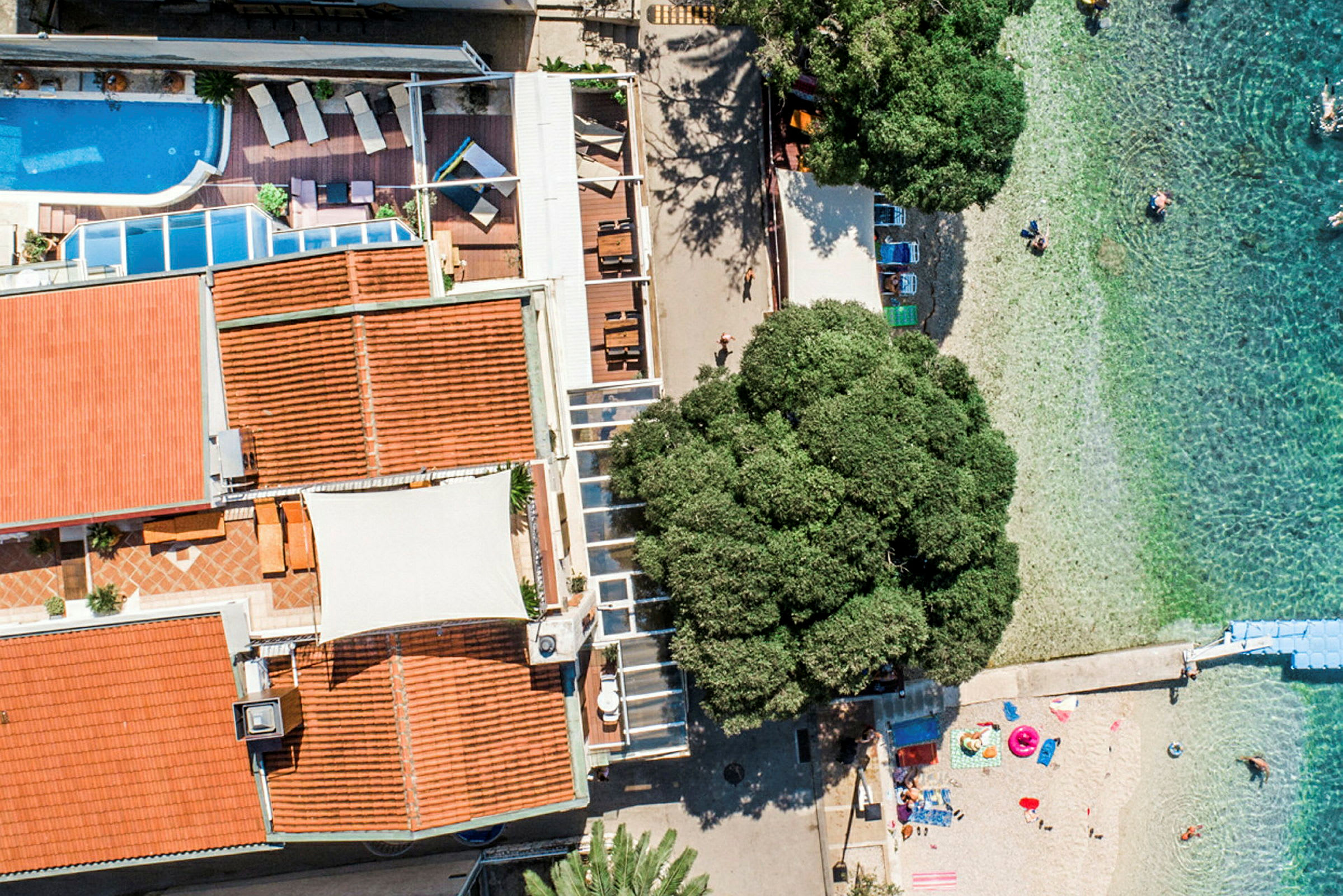 Flygfoto av en byggnad med pool och terrass bredvid en strand med klart vatten. (AI-genererad text)