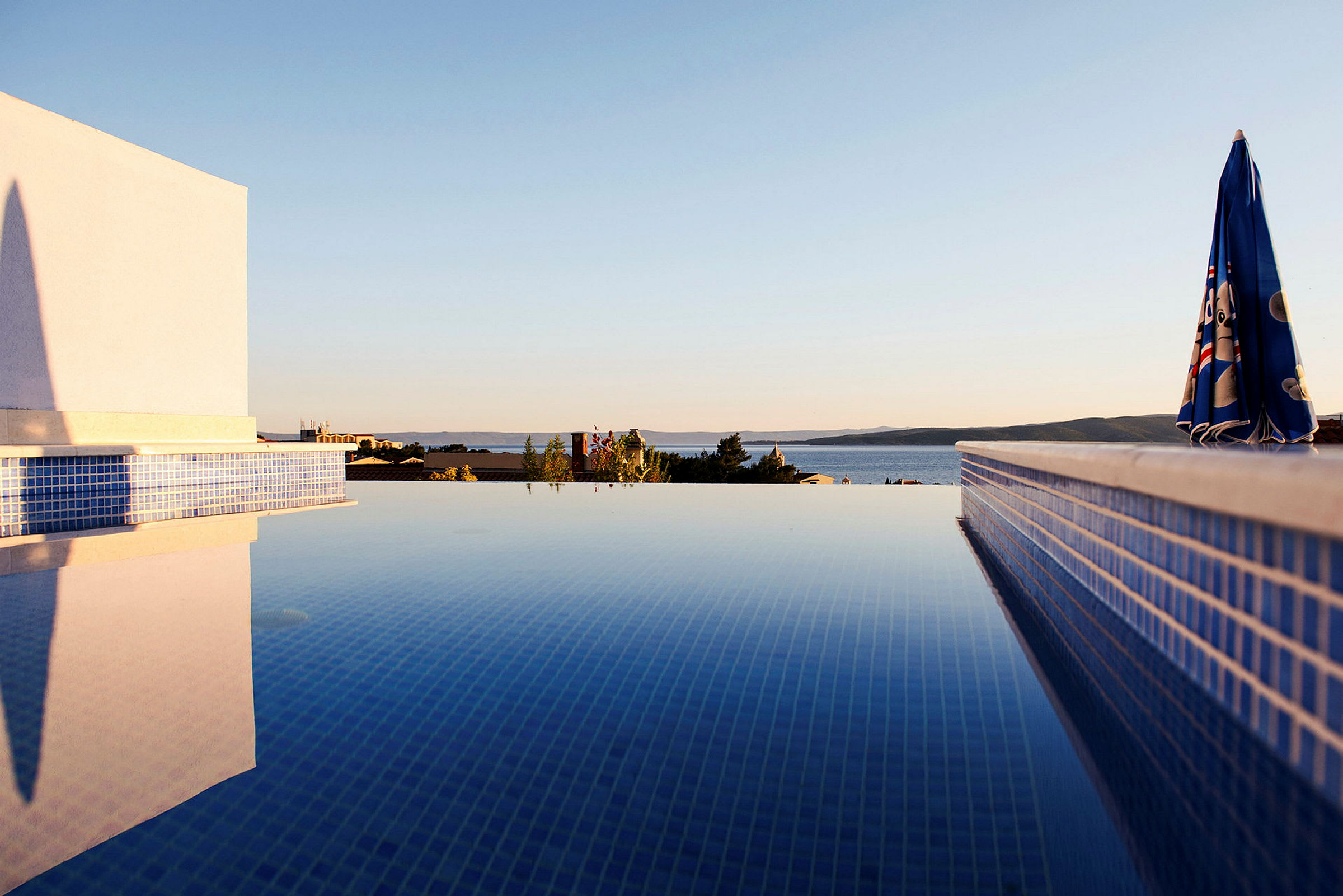Utsikt över en pool med klar himmel och bakgrund av hav och kullar. (AI-genererad text)