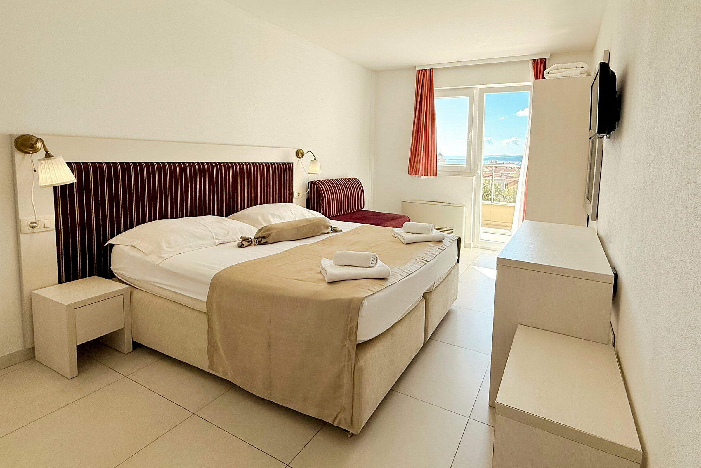 Ett hotellrum med en säng och sittplats med utsikt över terrass och hav. (AI-genererad text)