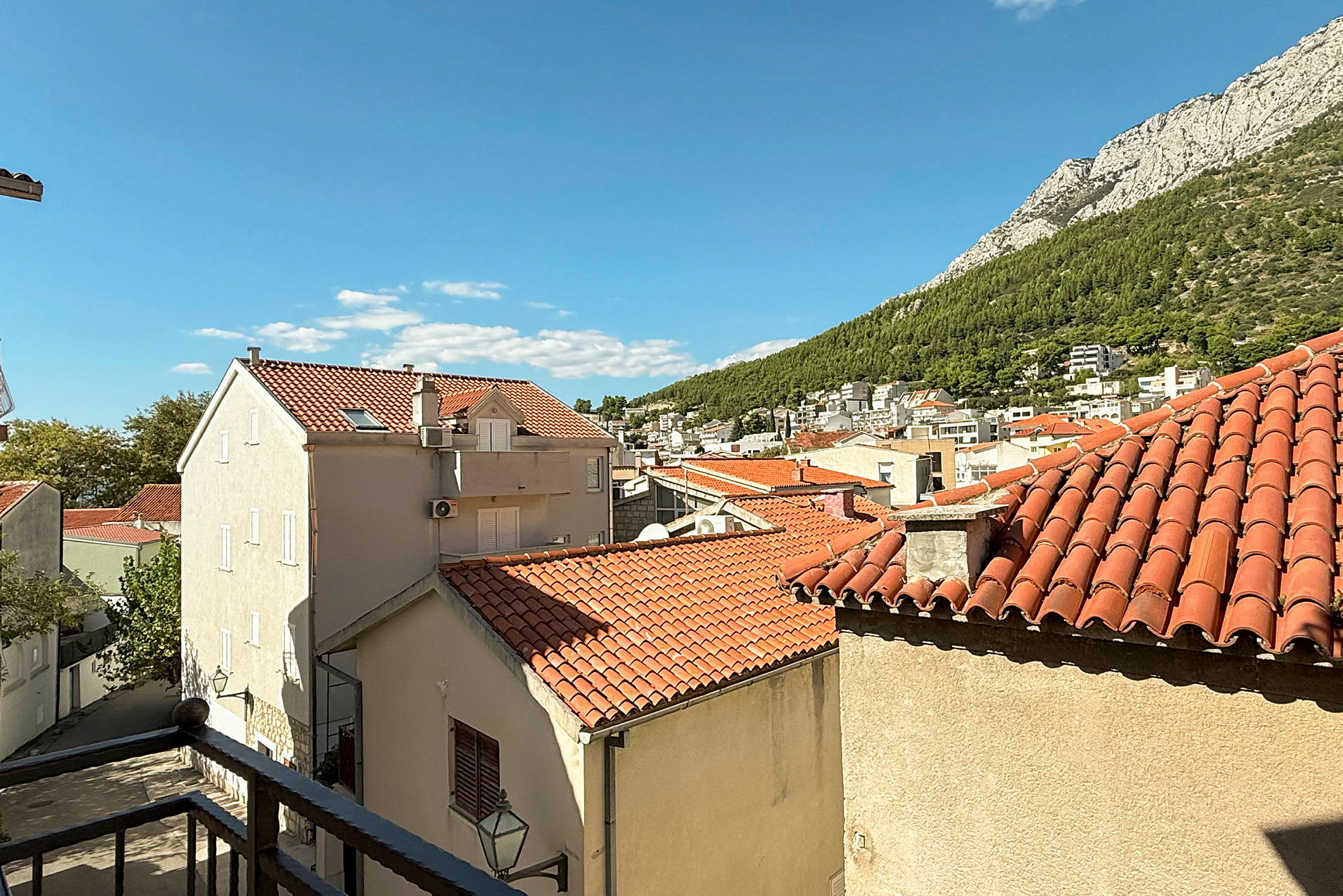 Vy över stadsbebyggelse med röda tegeltak och berg i bakgrunden. (AI-genererad text)