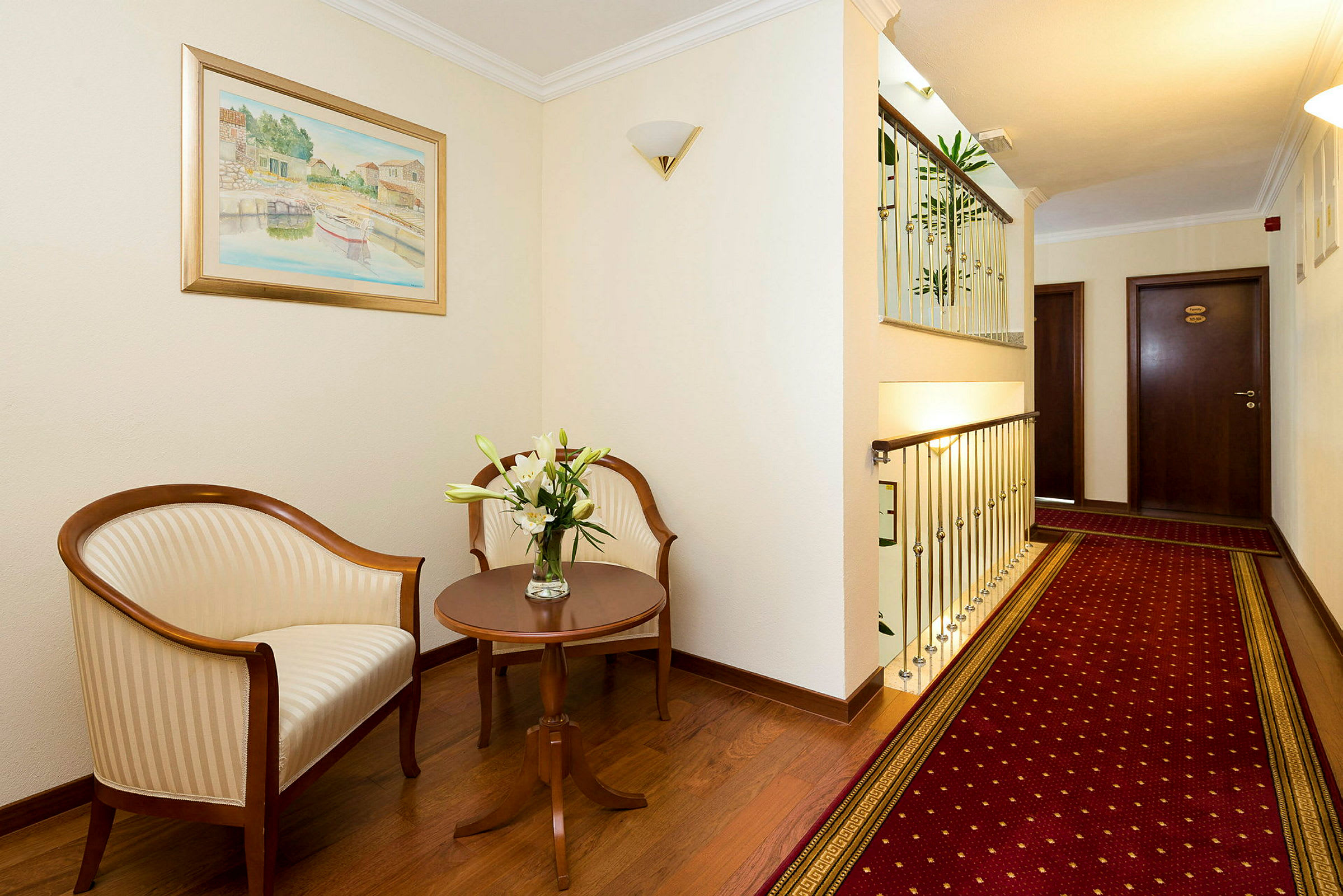 Bild av en hotellkorridor med sittområde, inklusive två stolar, ett sidobord med blommor och en röd matta. (AI-genererad text)