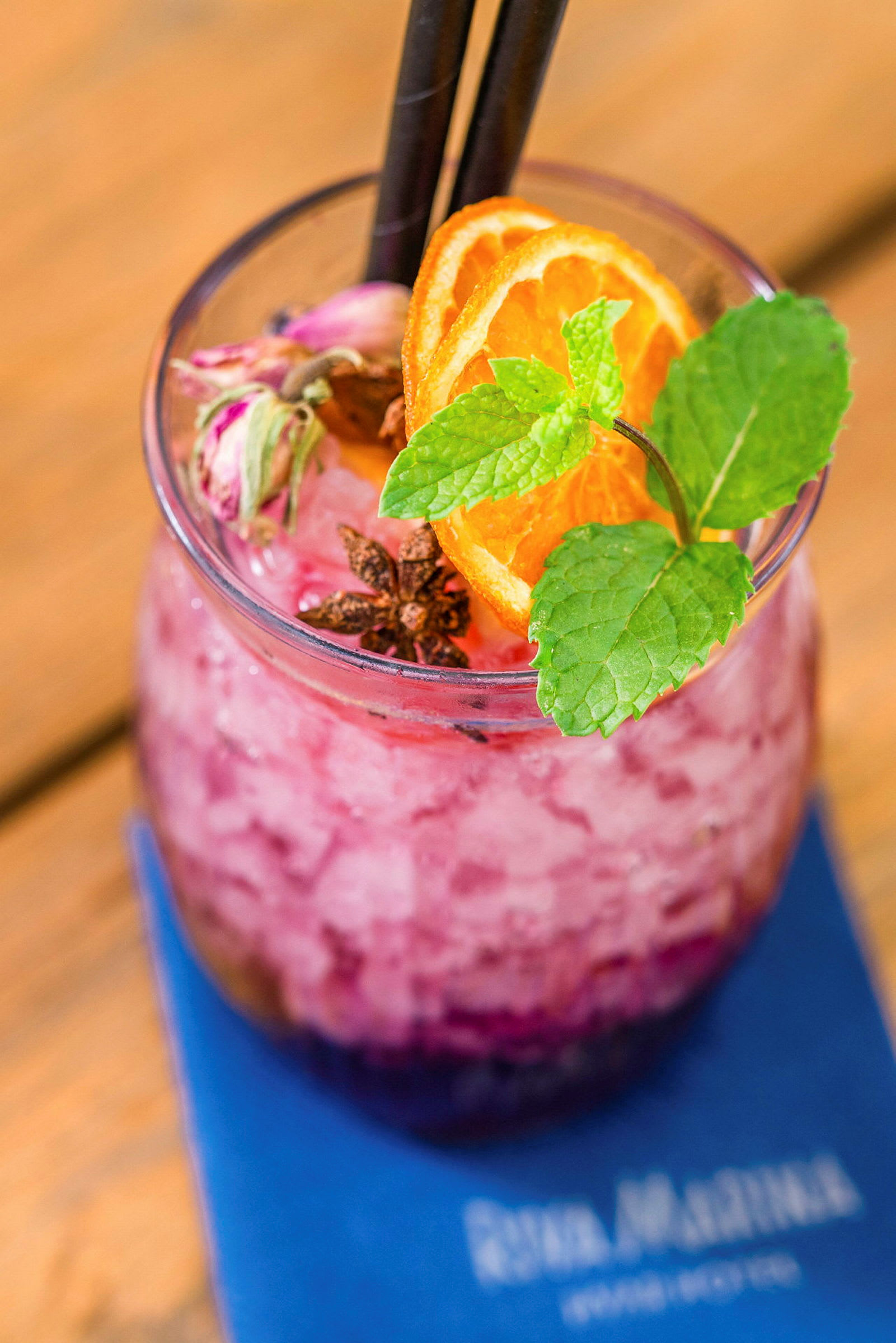 Ett glas med rosa krossad is och dekorationer av apelsinskivor, mynta och kryddor. (AI-genererad text)