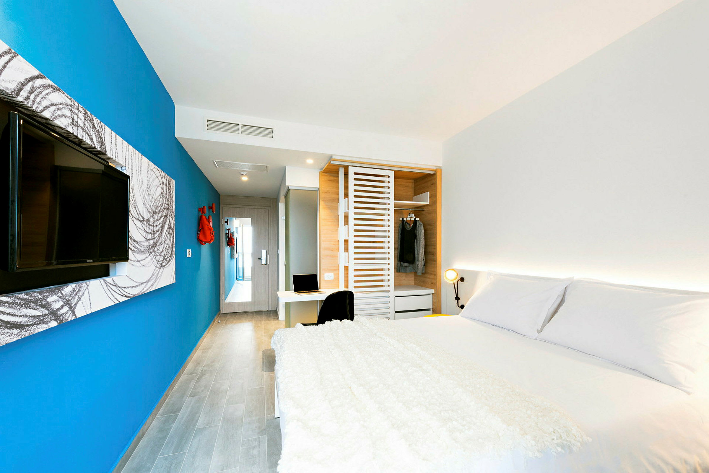 Ett modernt hotellrum med en stor säng, blå vägg, TV, garderob och ett skrivbord. (AI-genererad text)