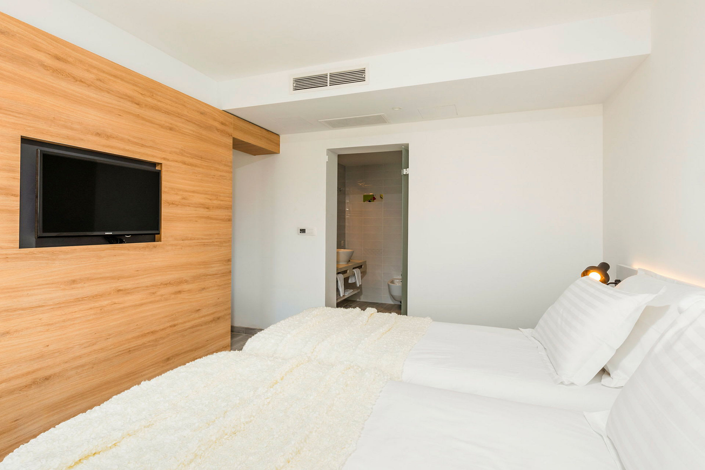 Ett hotellrum med två enkelsängar, en väggmonterad TV och en öppen dörr till badrummet. (AI-genererad text)