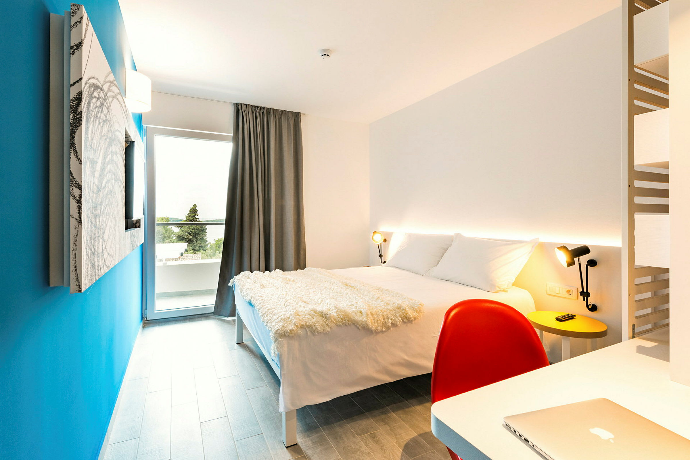 Modernt inrett hotellrum med en dubbelsäng, skrivbord och en blå vägg. (AI-genererad text)