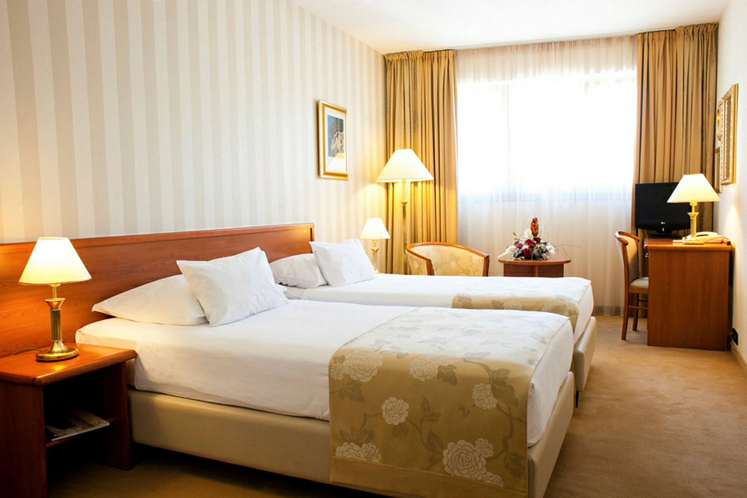 Ett hotellrum med två enkelsängar, lampor bredvid sängarna och ett skrivbord med stol. (AI-genererad text)