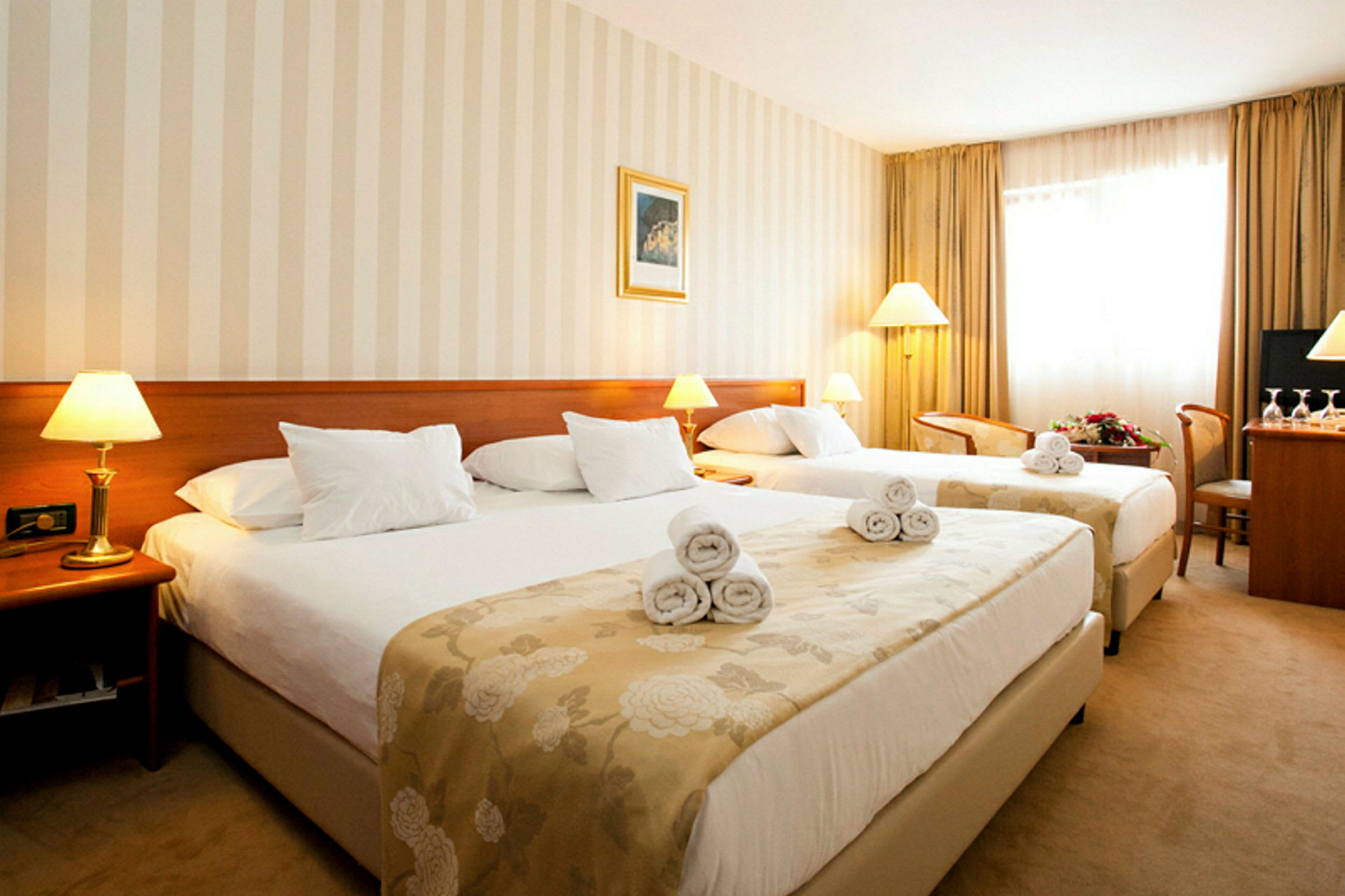Ett hotellrum med två sängar försedda med vita sängkläder och handdukar. Varm belysning från bordslampor och en golvlampa. (AI-genererad text)