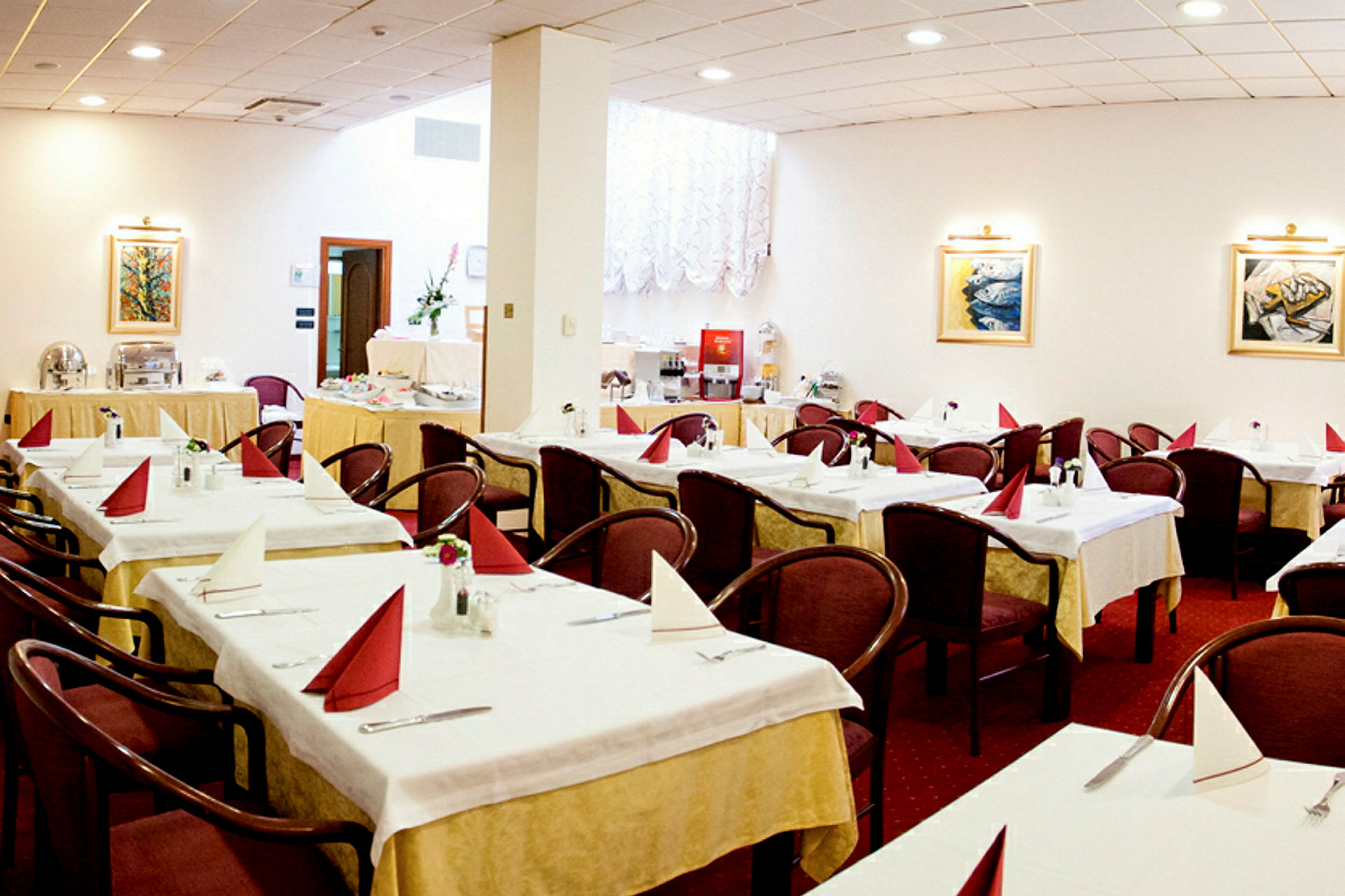 En restauranginteriör med flera uppsatta bord, var och en bestyckad med vikta servetter och stolar, samt dekorationer som tavlor och vägglampor. (AI-genererad text)
