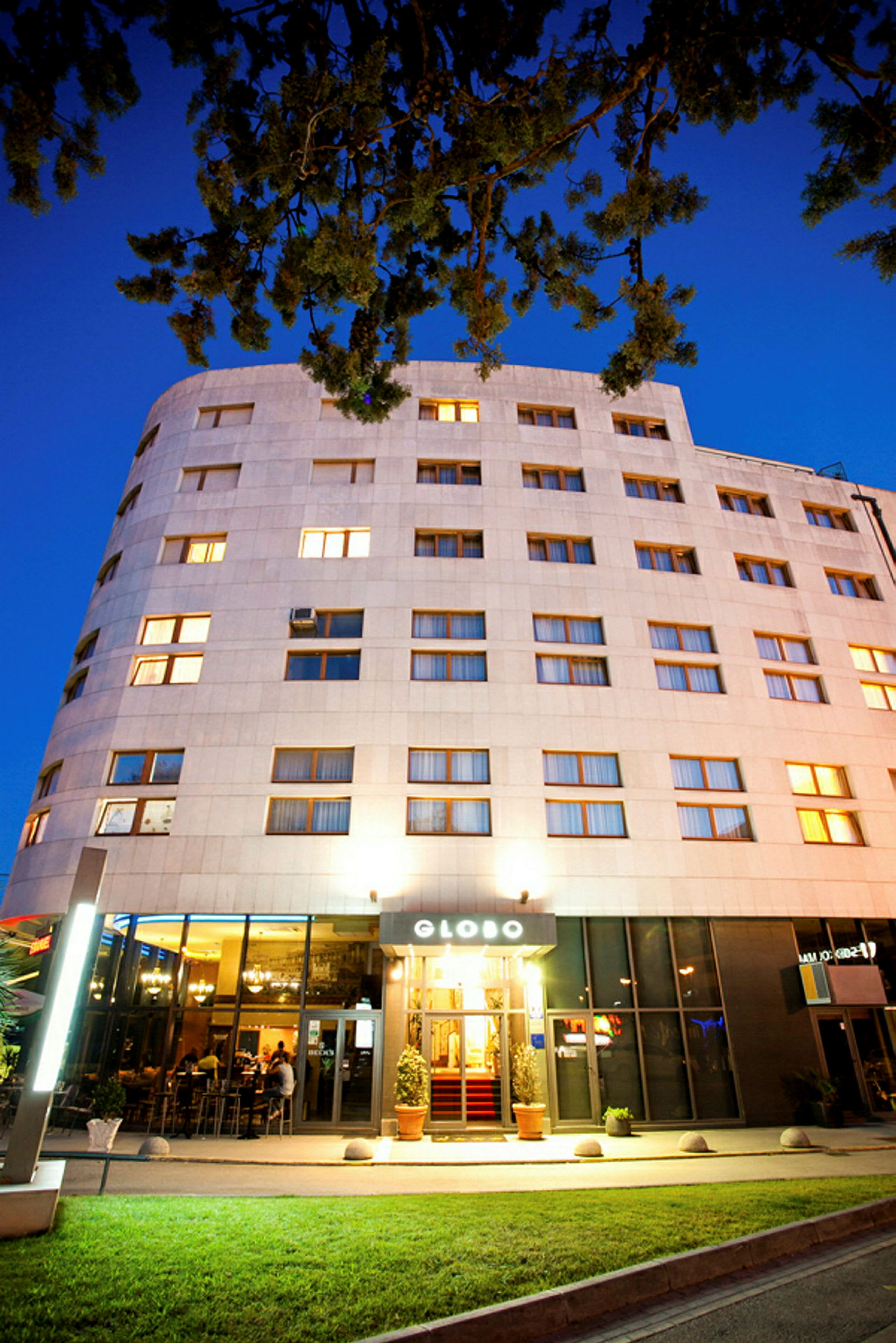 Ett hotell med upplyst fasad och entré, fotograferat i skymningen. (AI-genererad text)