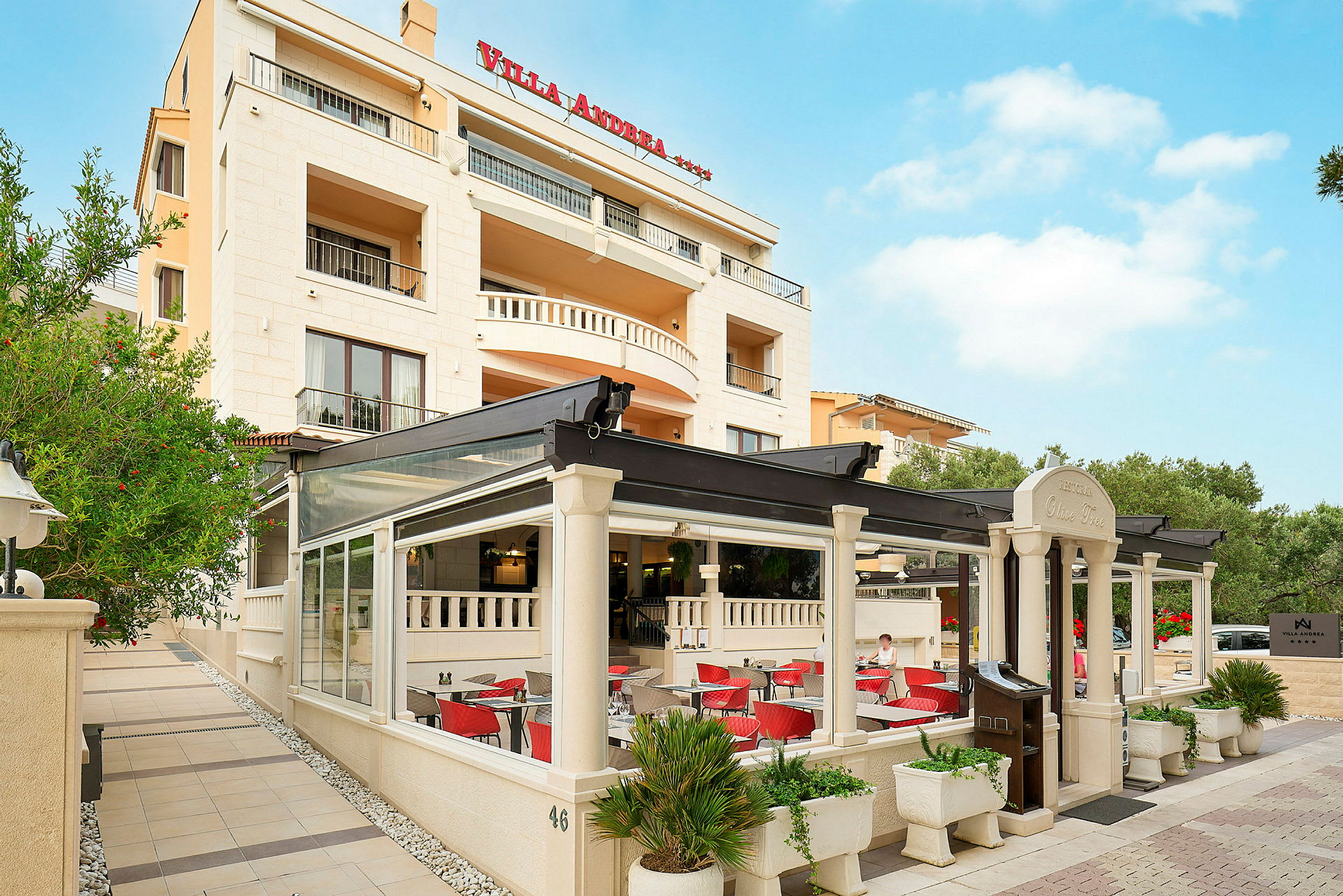 Fasaden av Villa Andrea hotell med en utomhusrestaurang. (AI-genererad text)