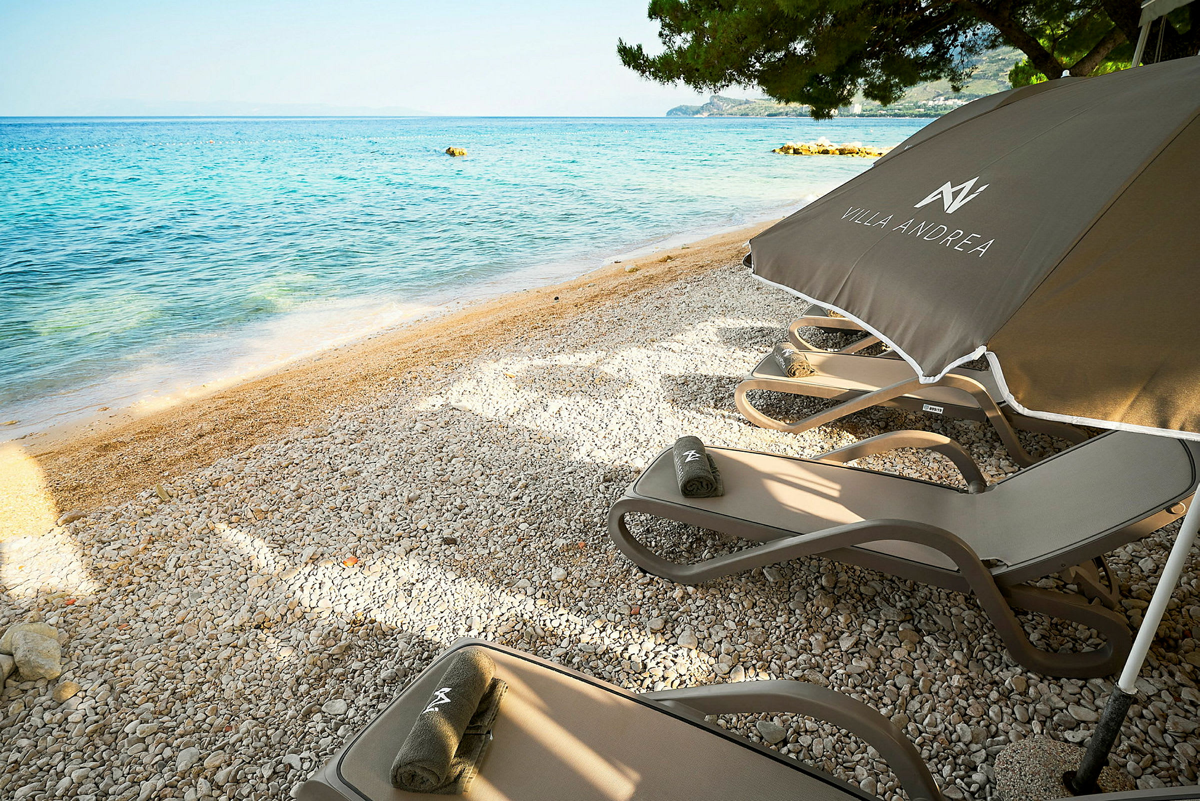 Solstolar och parasoll på en stenstrand med utsikt över havet. (AI-genererad text)