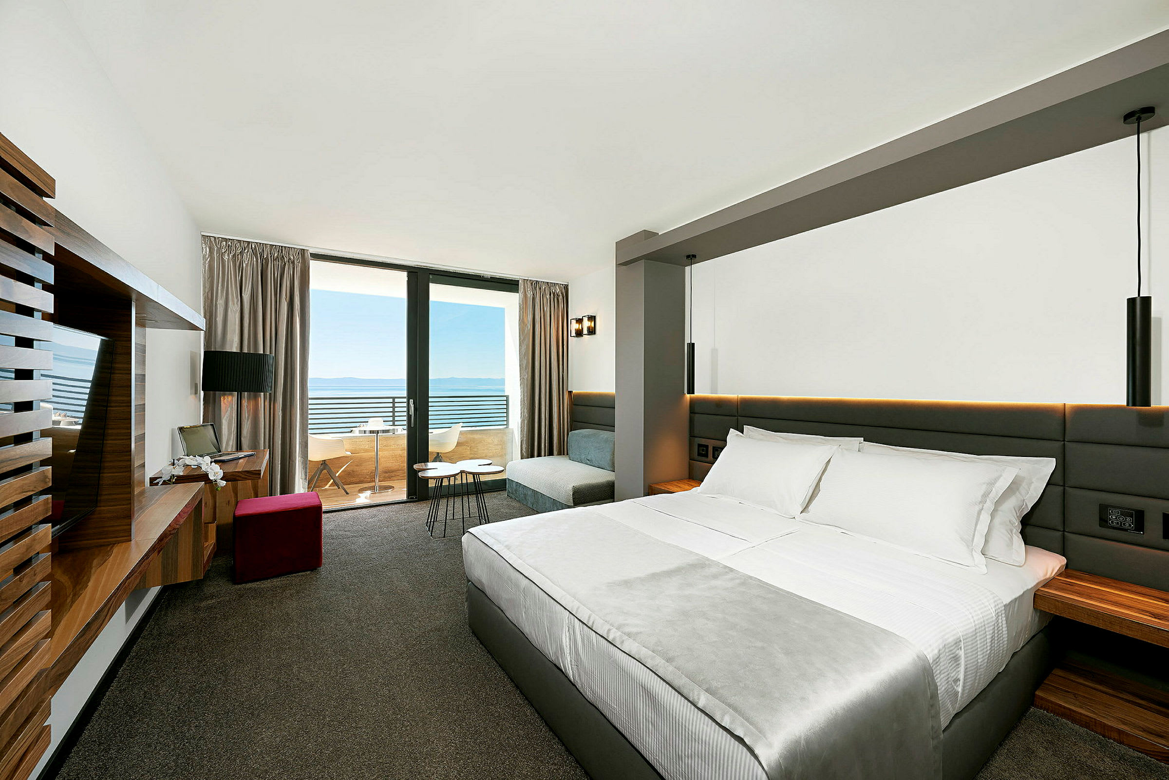 Ett hotellrum med säng, soffa och skrivbord, samt en balkong med utsikt över havet. (AI-genererad text)