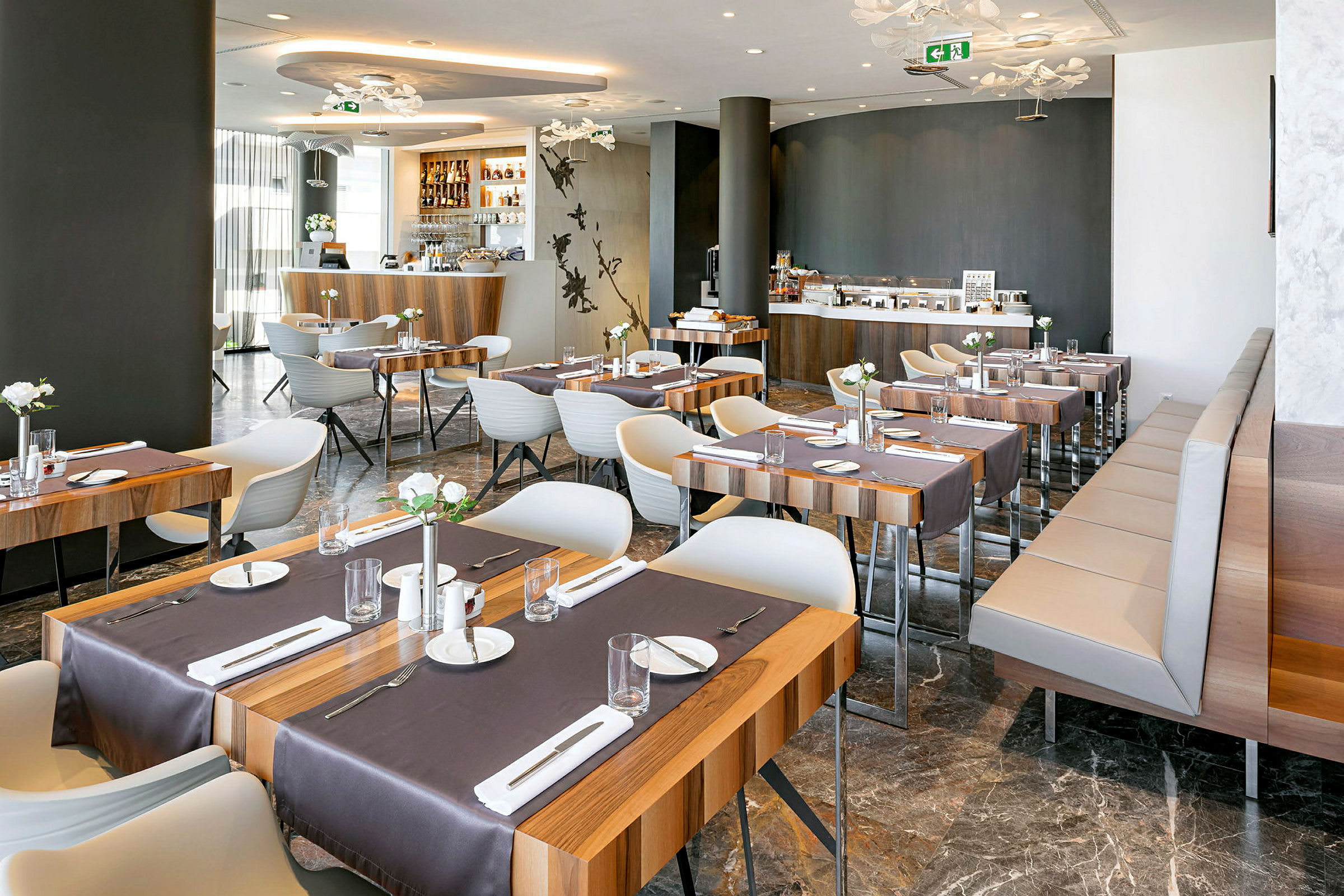 Ett modernt restaurangområde med träbord och vita stolar, dukade för måltider. (AI-genererad text)