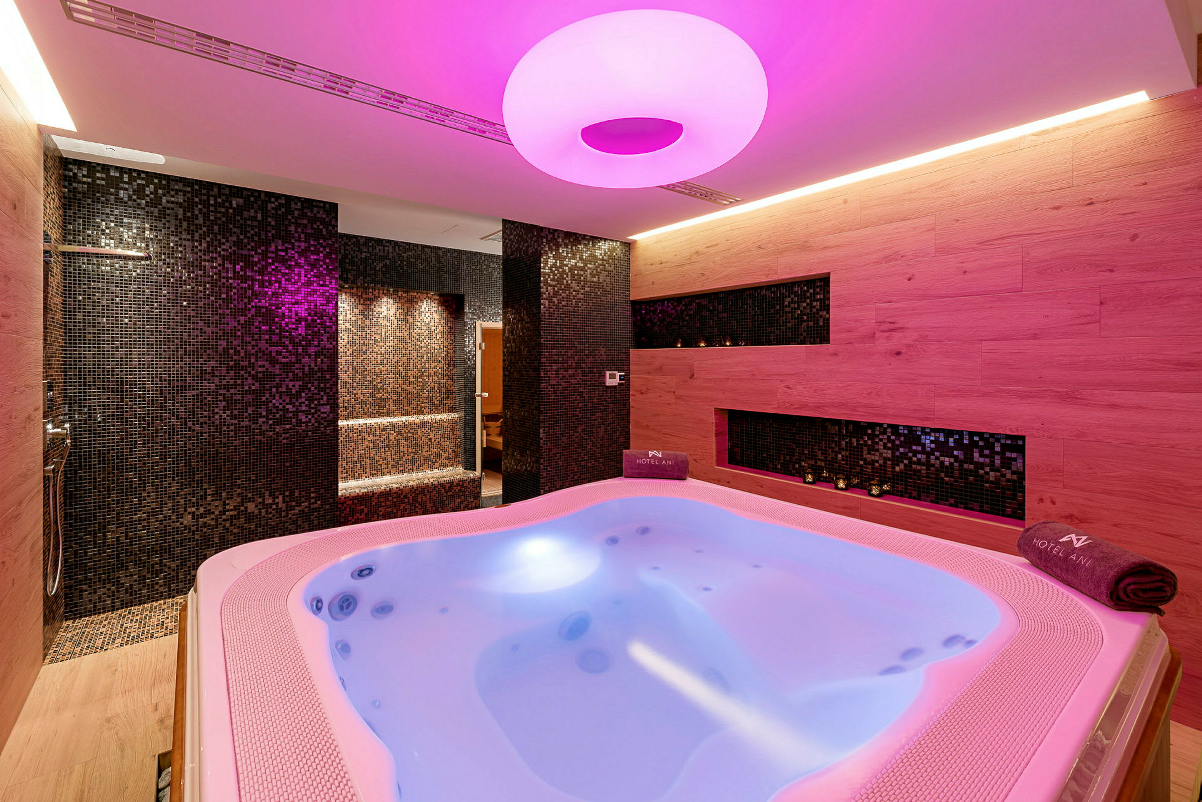 Bubbelpool med träpaneler och mosaikväggar, upplyst med rosa ljus. (AI-genererad text)