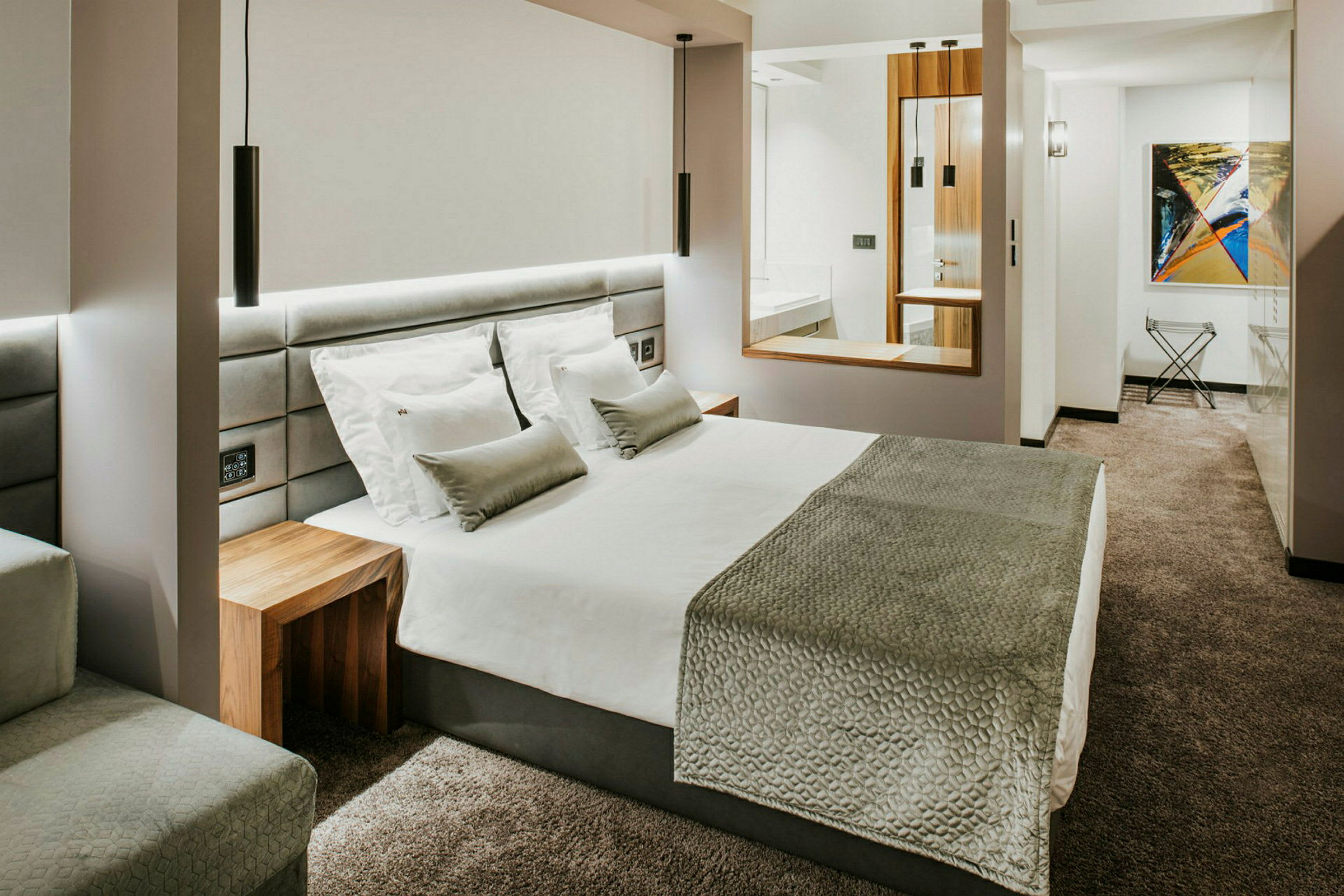 Ett modernt hotellrum med en stor säng, vit sängkläder, grå överkast och kuddar och ett grått heltäckningsmatta. (AI-genererad text)