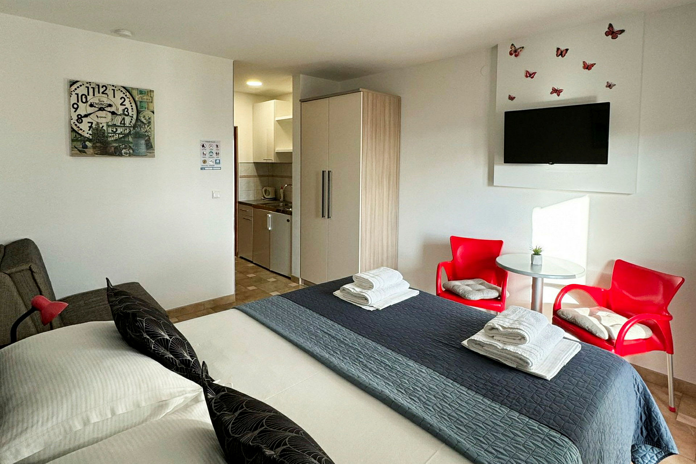 Ett hotellrum med en säng, röda stolar, bord, garderob och ett litet kök. (AI-genererad text)