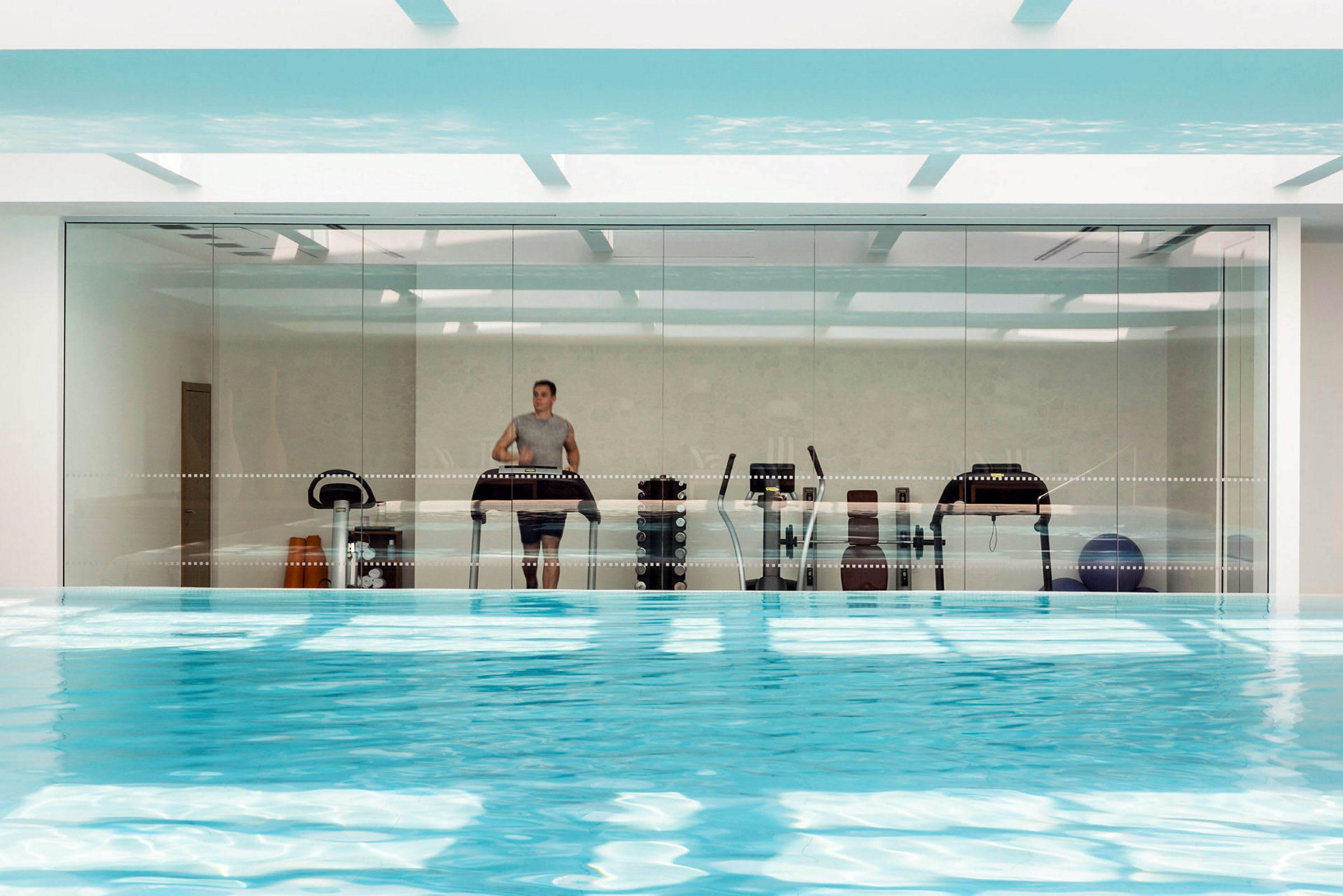 En inomhuspool med utsikt mot ett glasparti som visar träningsutrustning. (AI-genererad text)