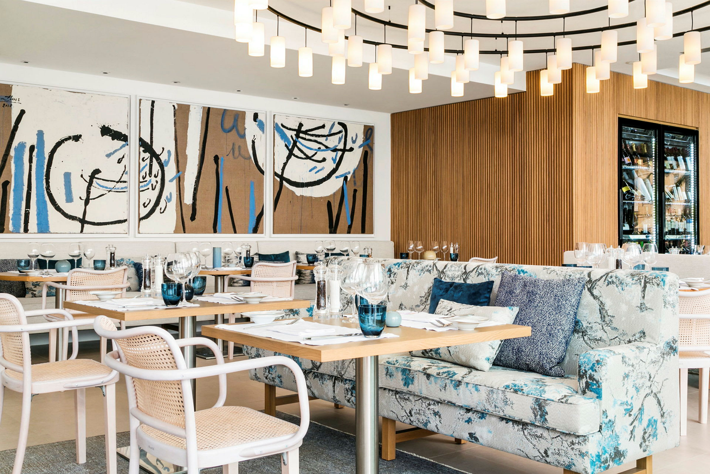 Ett elegant inrett restaurangområde med moderna konstverk på väggen, en stor ljuskrona, bekväma stolar och soffor samt uppsatta bord. (AI-genererad text)