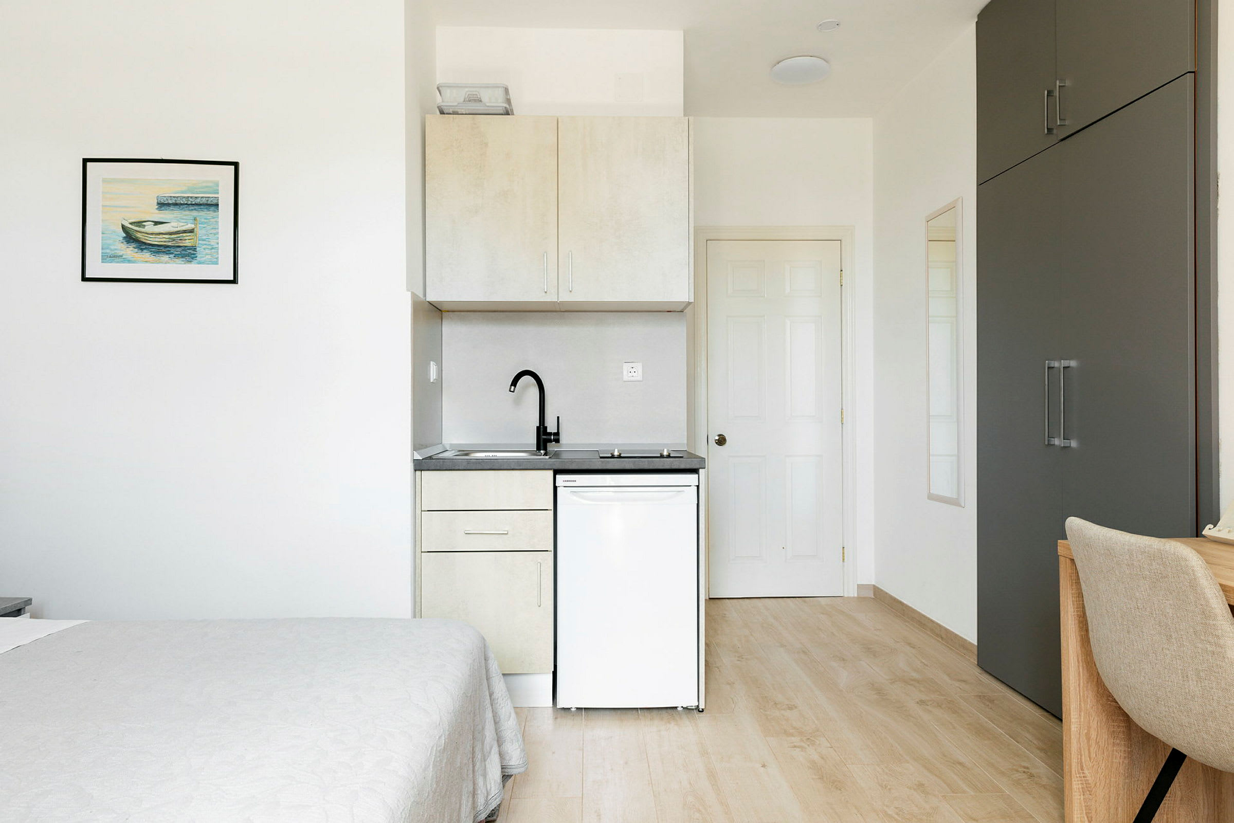 Väldesignat rum med minimalistisk interiör inklusive en säng, kitchenette, garderob och skrivbordsstol. (AI-genererad text)