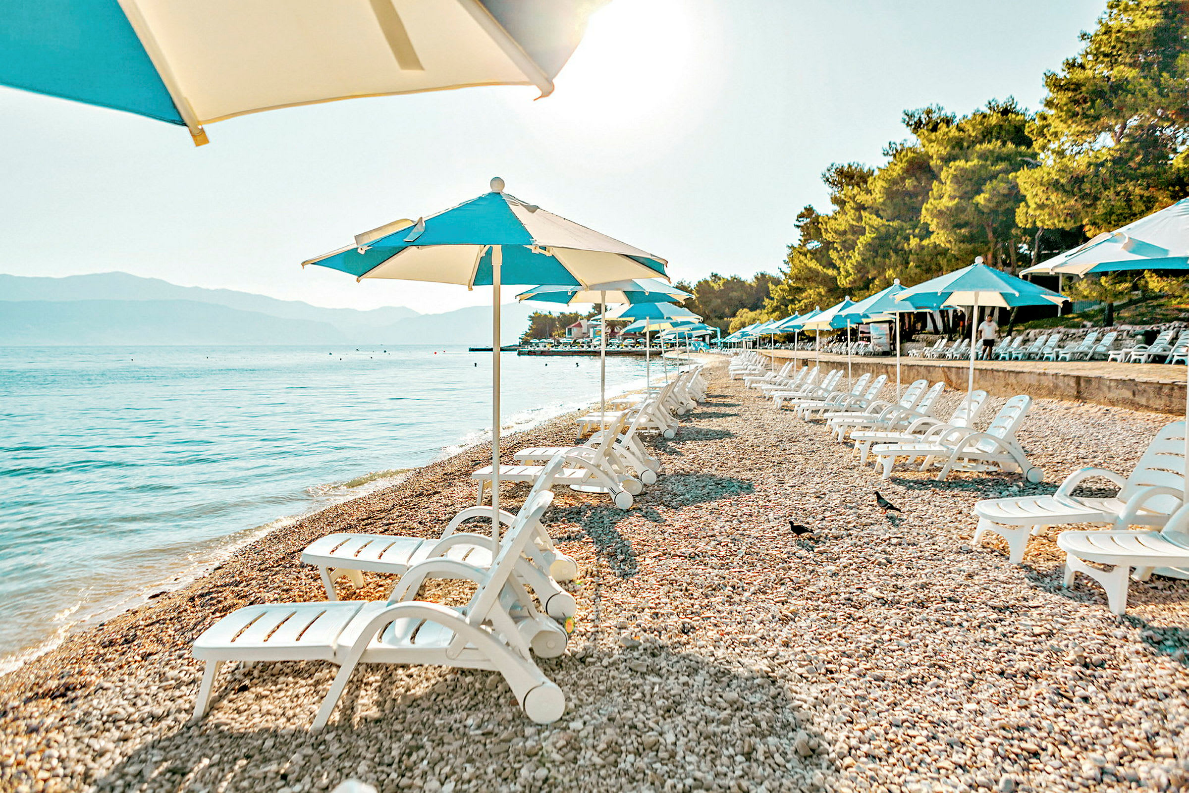 Solstolar och parasoller på en stenstrand bredvid havet. (AI-genererad text)