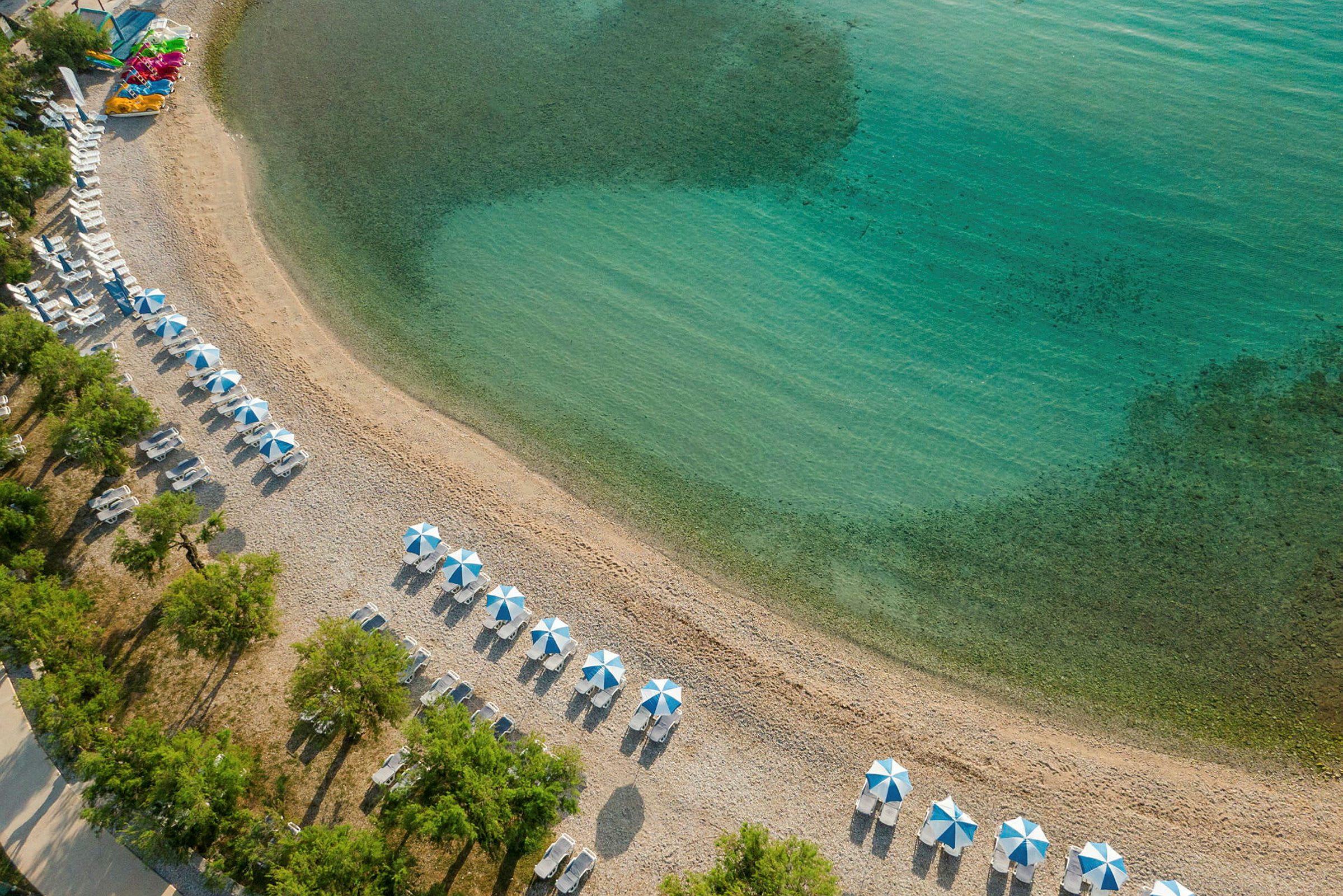 Flygvy över strand med parasoll och solstolar vid klart vatten. (AI-genererad text)