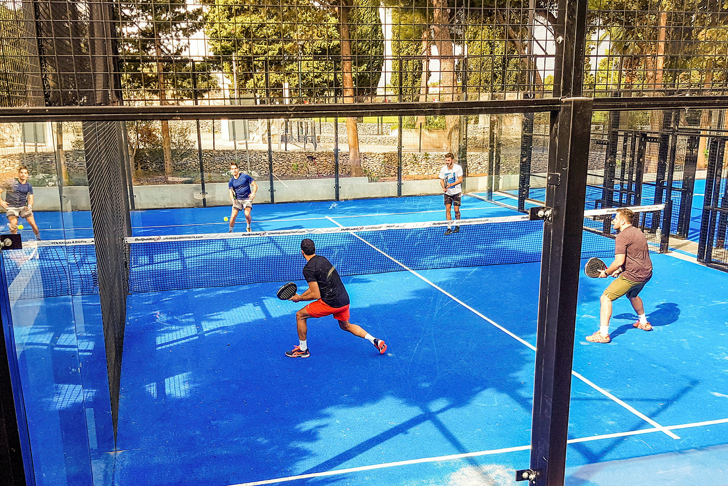 Fyra personer spelar padel på en blå plan med nät i mitten. (AI-genererad text)