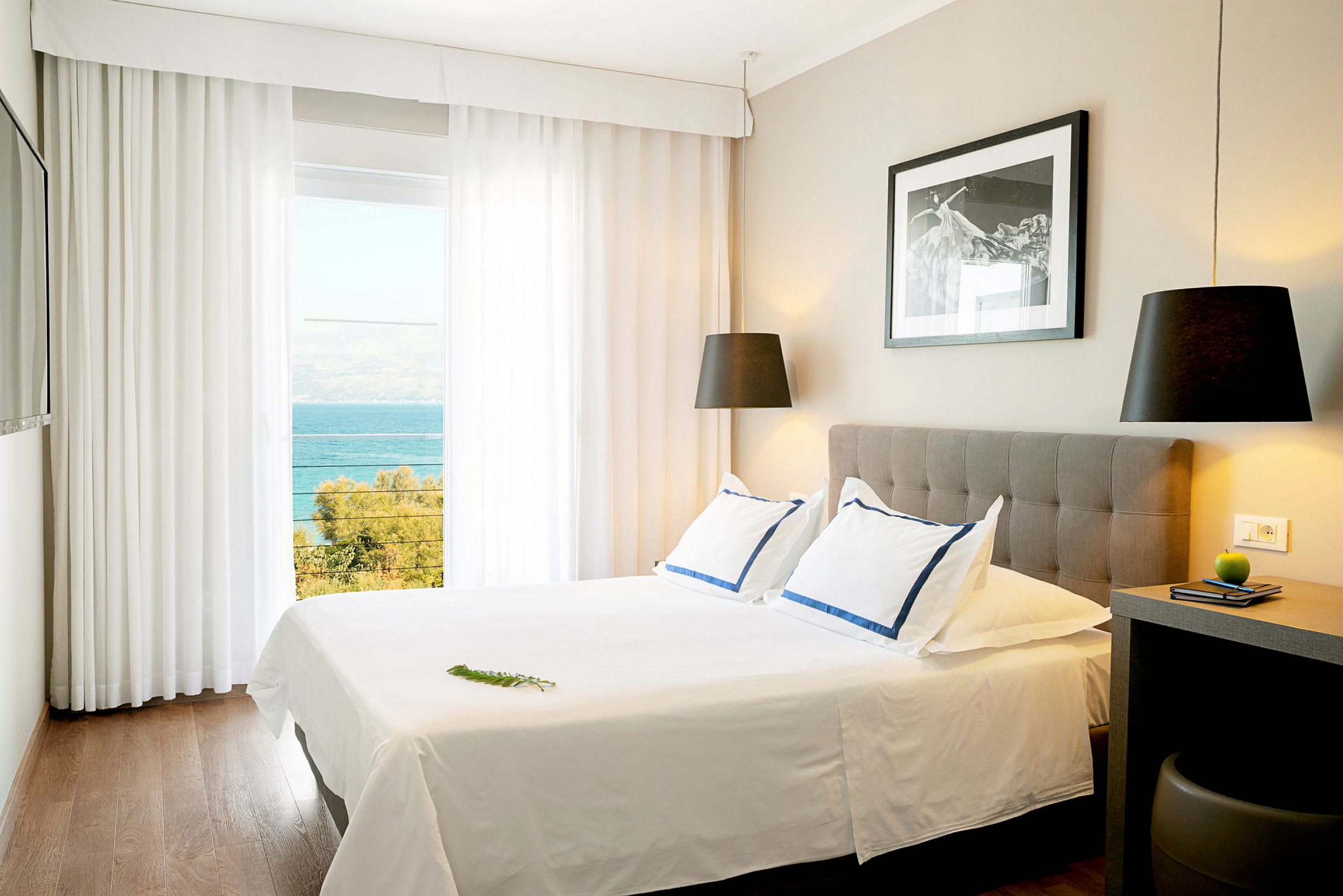 Ett ljust hotellrum med en dubbelssäng, modern inredning och havsutsikt genom stora fönster. (AI-genererad text)