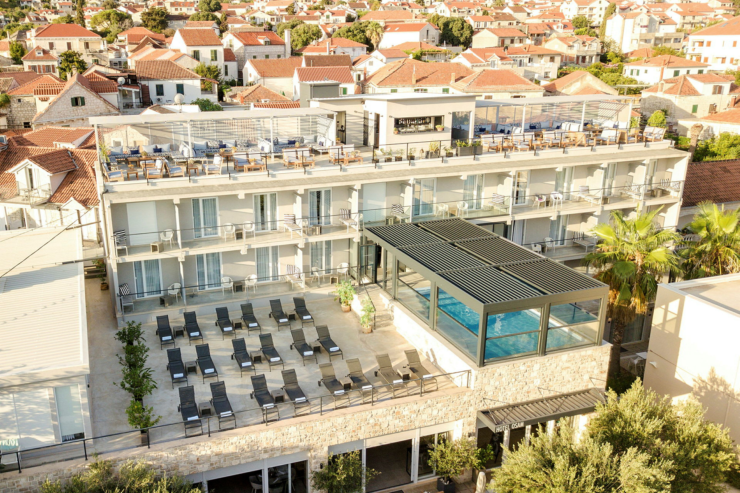 Vy över hotell med pool och solstolar samt takterrass i en stadsmiljö. (AI-genererad text)