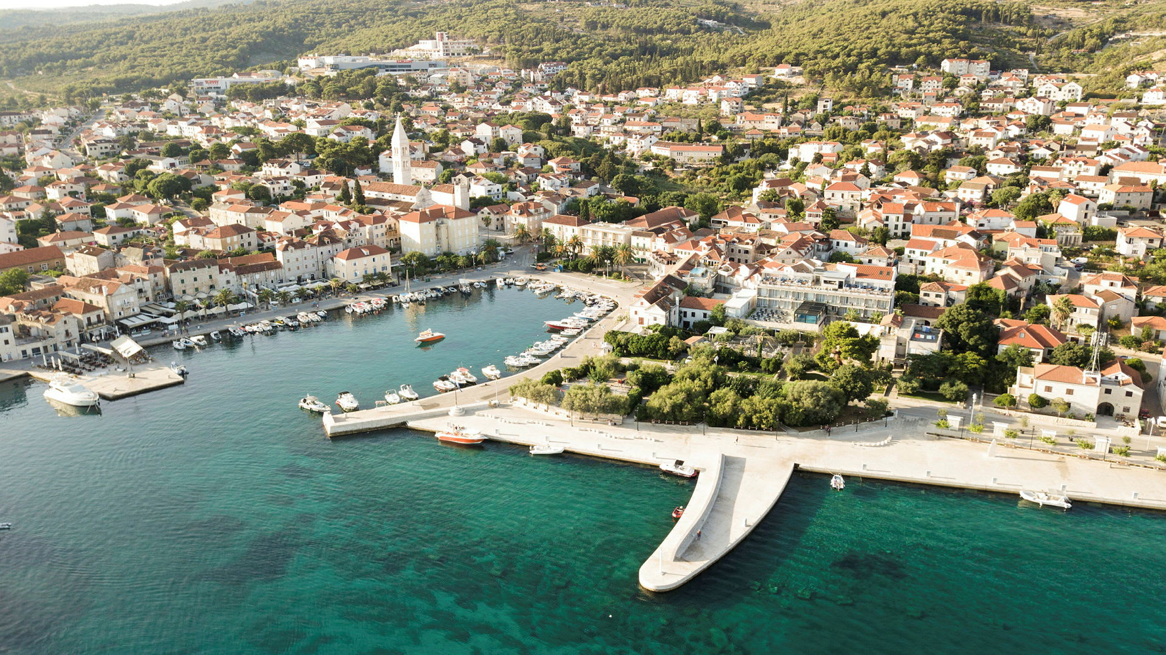 Flygfoto av en kuststad med båtar i en hamn och hus med röda tak. (AI-genererad text)