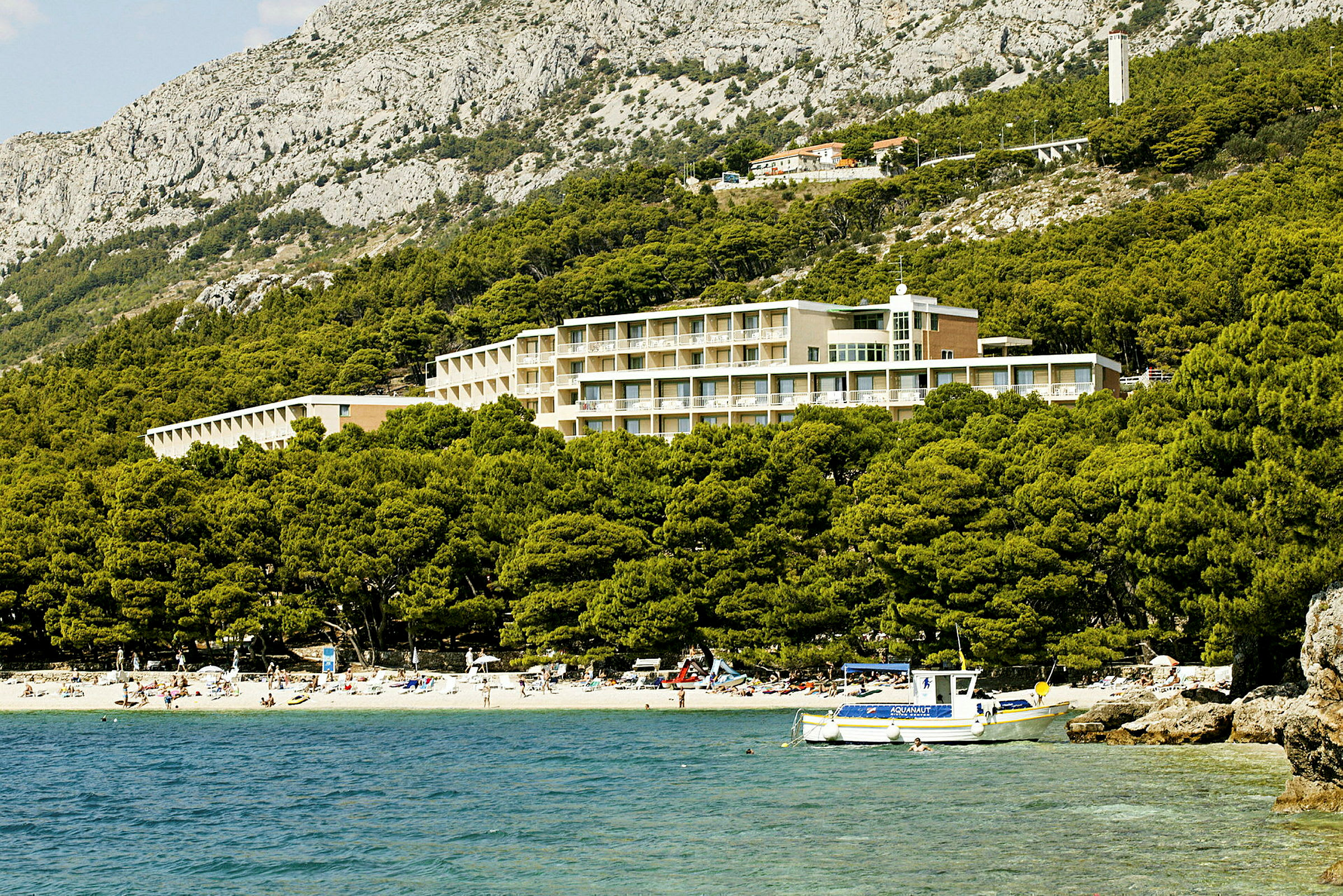 Hotell beläget vid en tallskog och strand i ett bergigt landskap. (AI-genererad text)