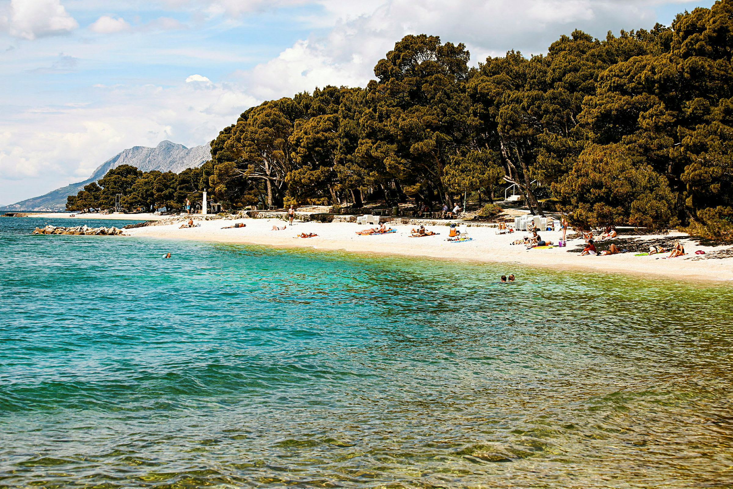 En strand med klart vatten och personer som solar på sanden. (AI-genererad text)