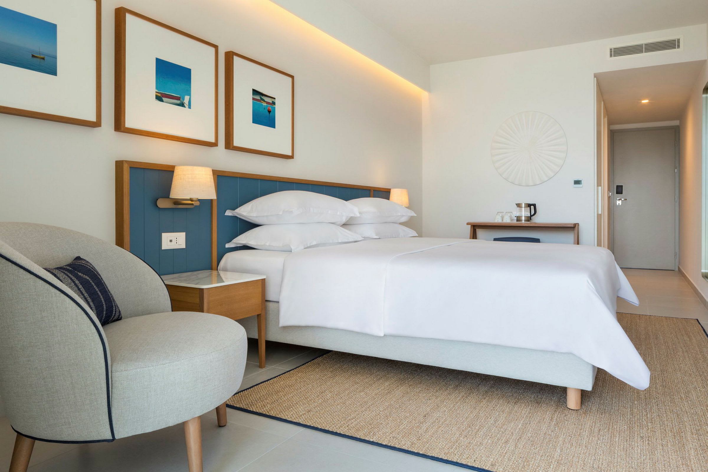 Ett hotellrum med en säng, nattduksbord, en fåtölj, en dörr och dekorativa väggdetaljer. (AI-genererad text)