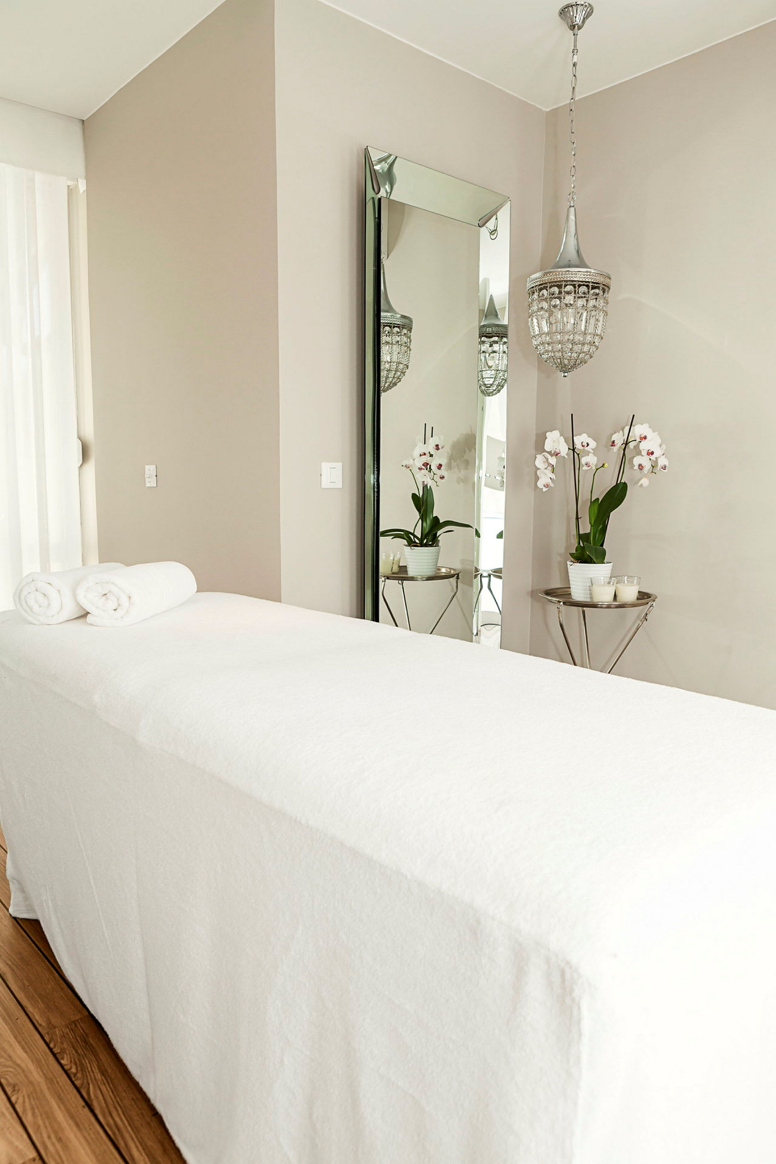 En massagebänk med vita handdukar, bakom finns en spegel, en kristallkrona och en bord med en vas med orkidéer. (AI-genererad text)
