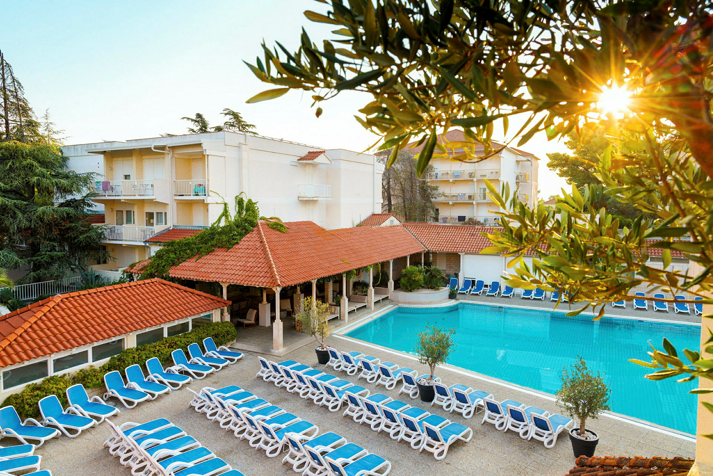 Bild av hotellområde med solstolar, pool och byggnader. (AI-genererad text)