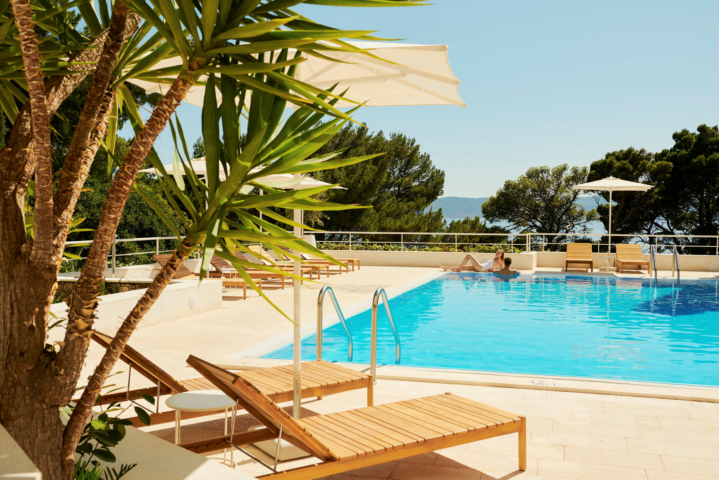 Pool med solstolar och parasoller, omgivet av träd. (AI-genererad text)
