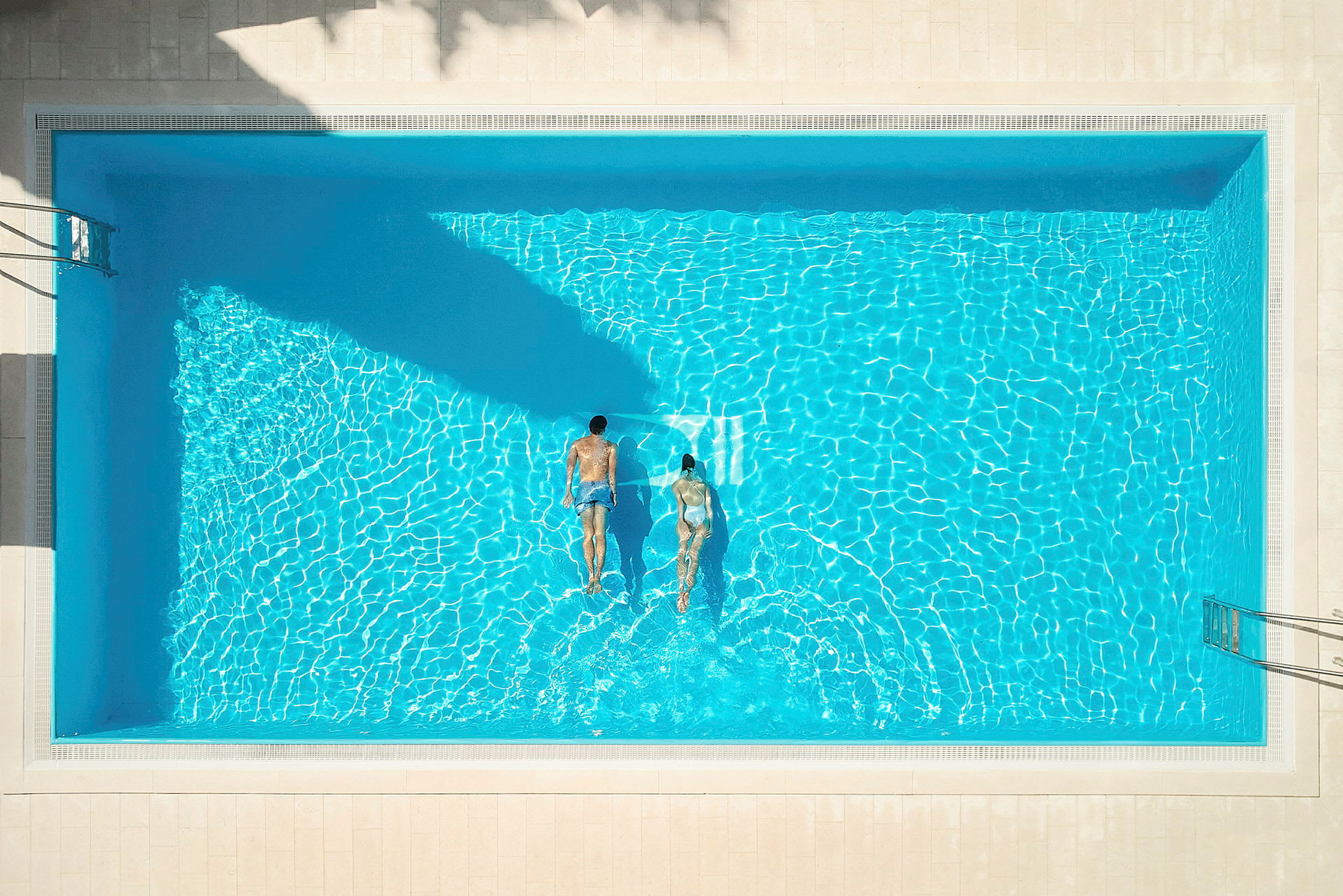 Två personer simmar i en pool, sedd från ovan. (AI-genererad text)