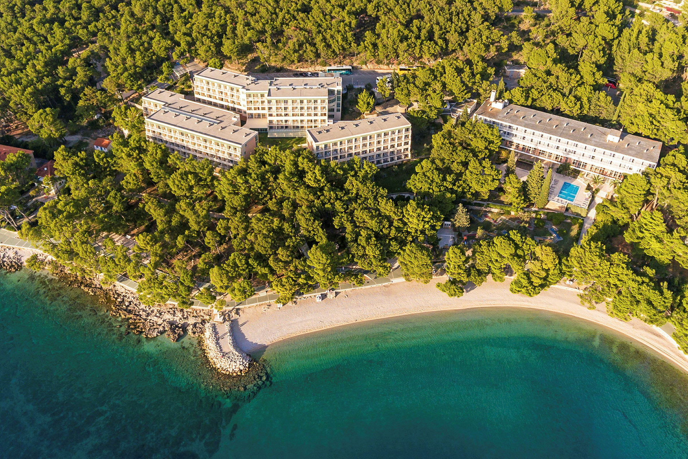 Flygbild över hotellkomplex omgivet av skog och strand. (AI-genererad text)