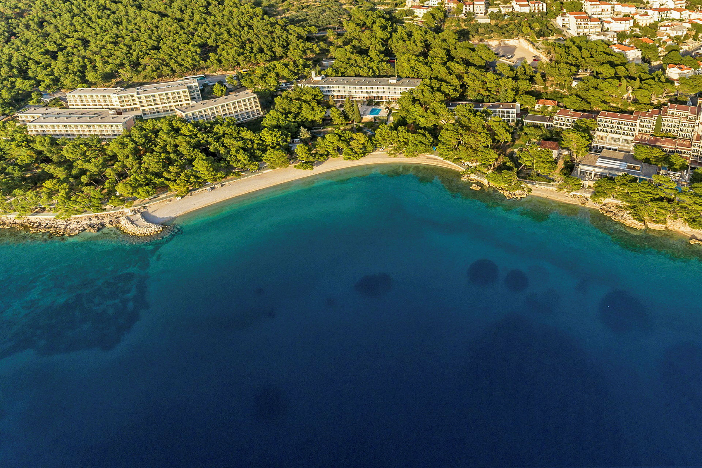 Flygvy över hotell vid kusten med strand och klart vatten. (AI-genererad text)