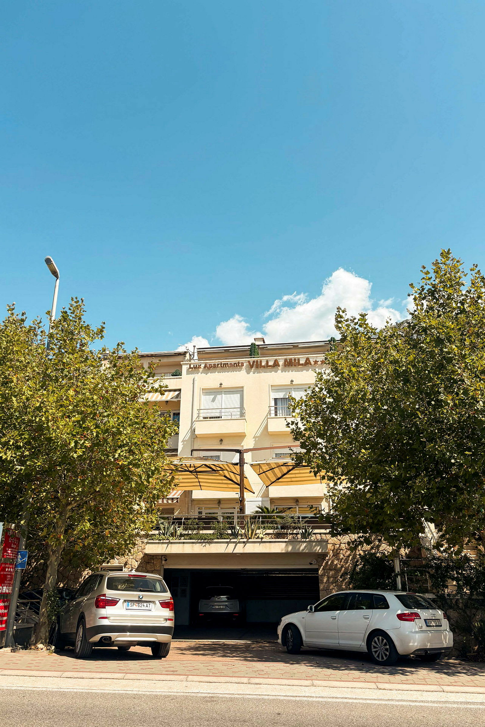 En byggnad med parkerade bilar framför och skylt som säger 'Villa Mila'. (AI-genererad text)