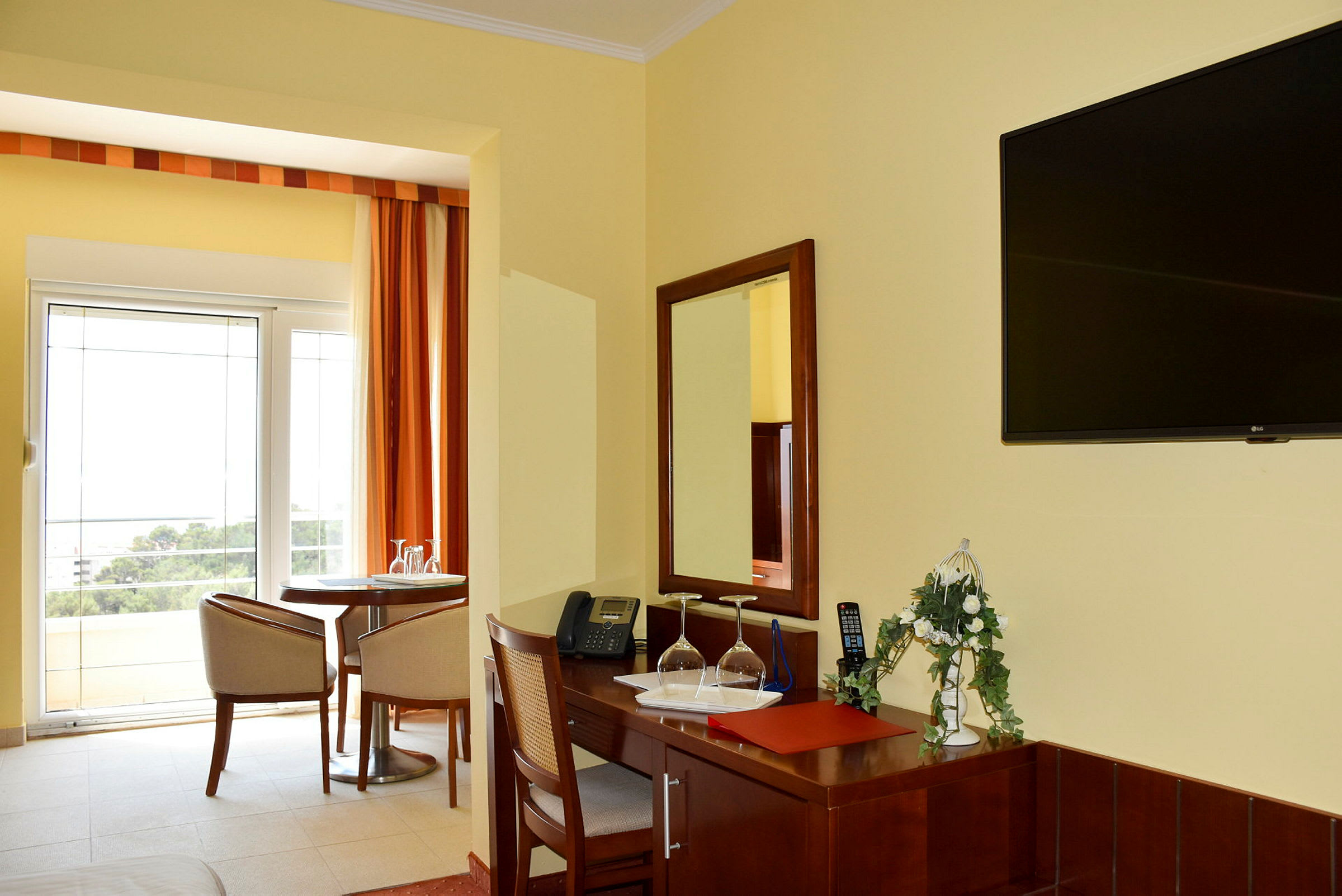 Hotellrum med skrivbord, sittgrupp och utsikt mot balkong. (AI-genererad text)