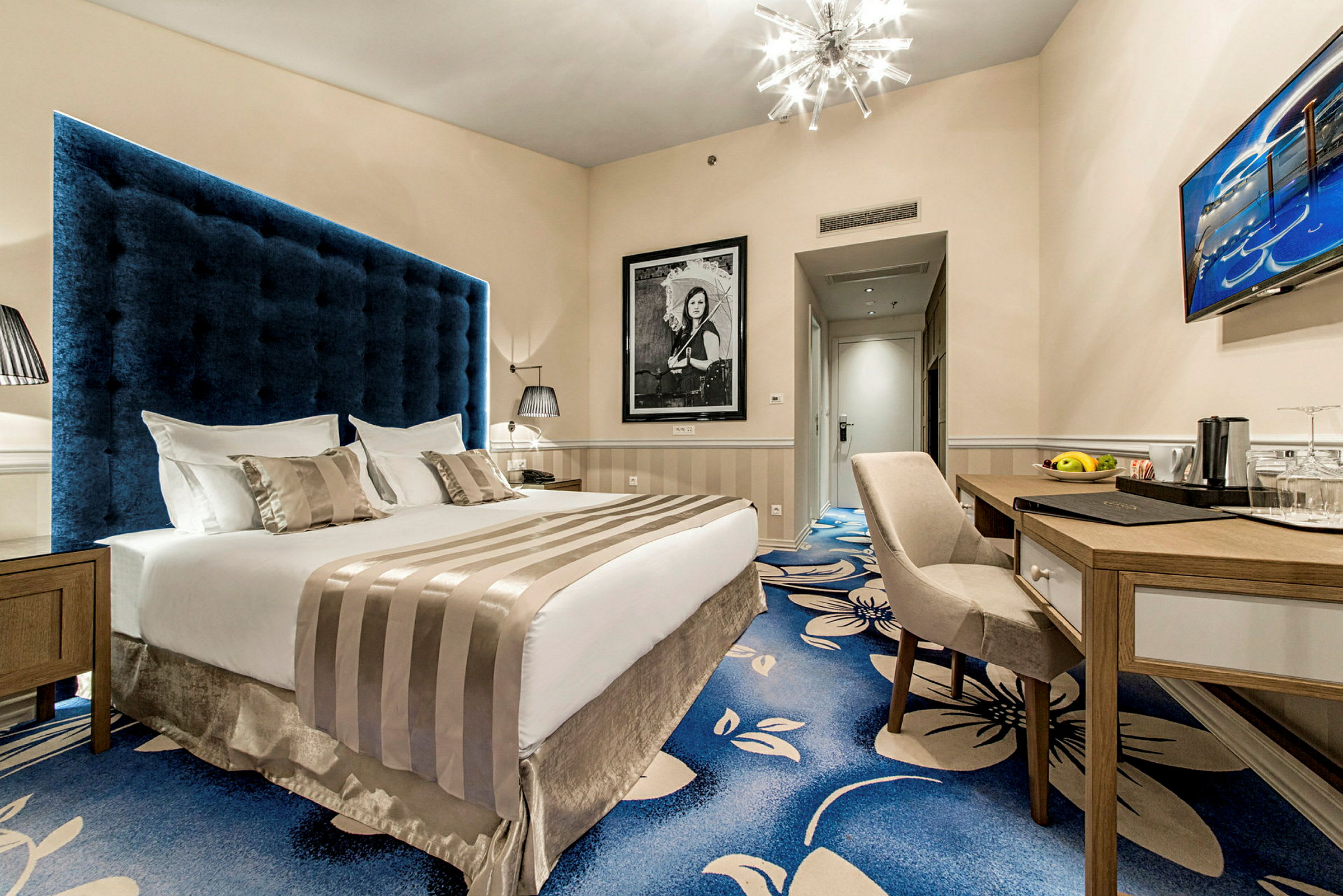 Hotellrum med en stor säng, skrivbord och stol, samt ett blått och blommigt golv. (AI-genererad text)