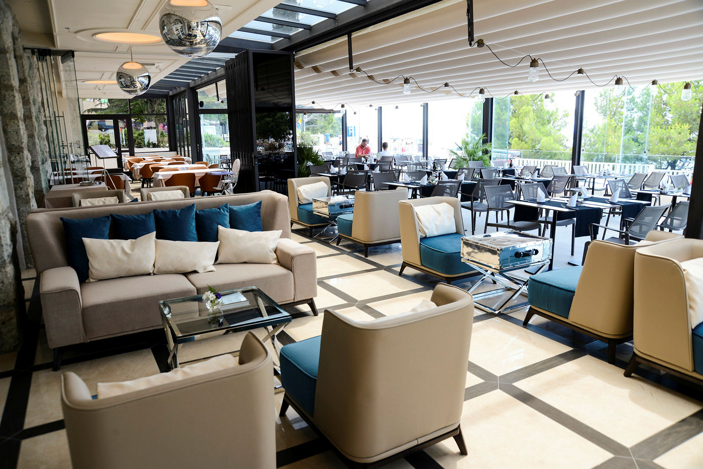 En modern loungemiljö med soffor, sittplatser och bord. Stora fönster med utsikt mot trädgård. (AI-genererad text)
